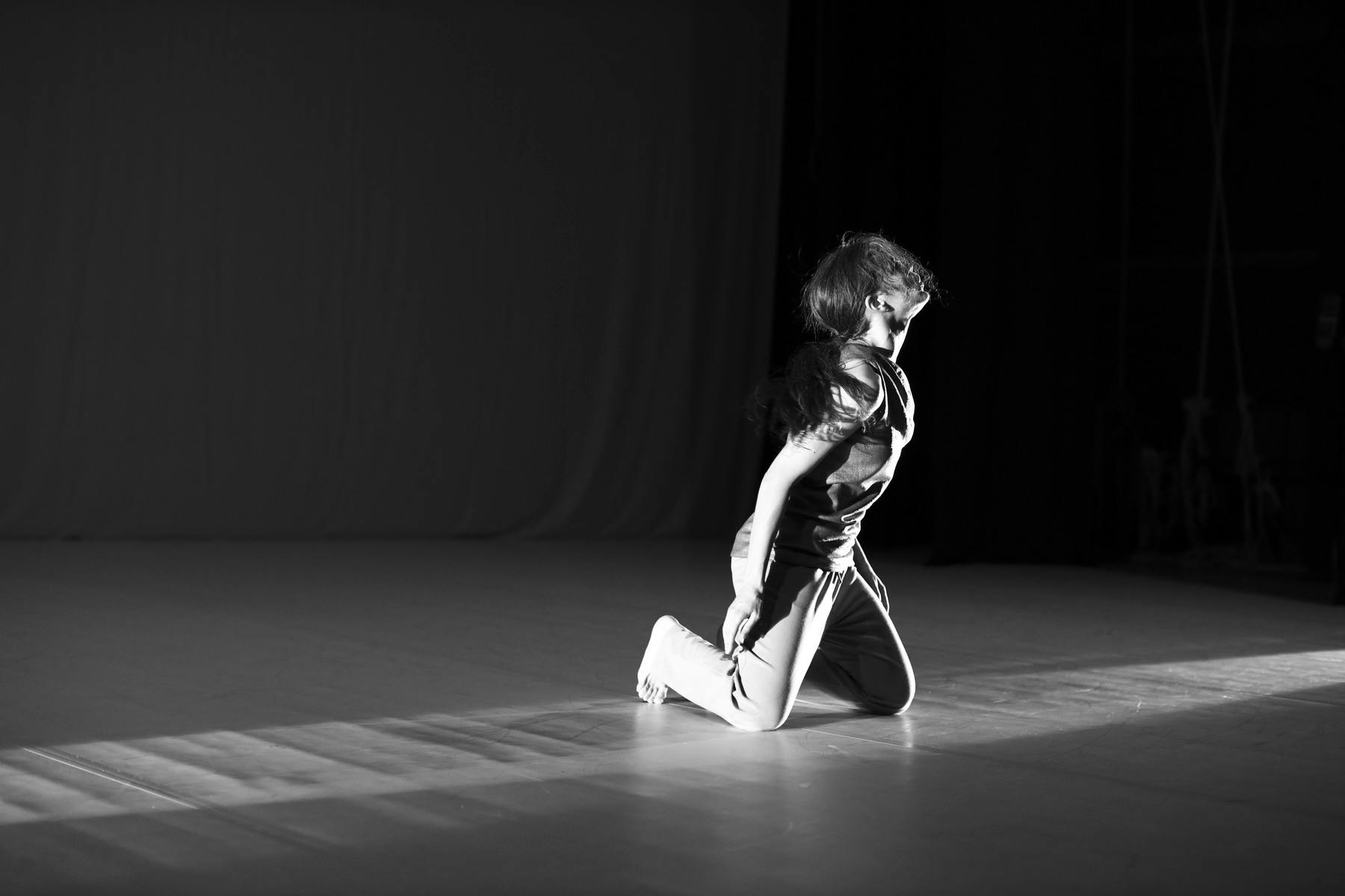 Foto in bianco e nero di performer inginocchiata che guarda alla sua sinistra