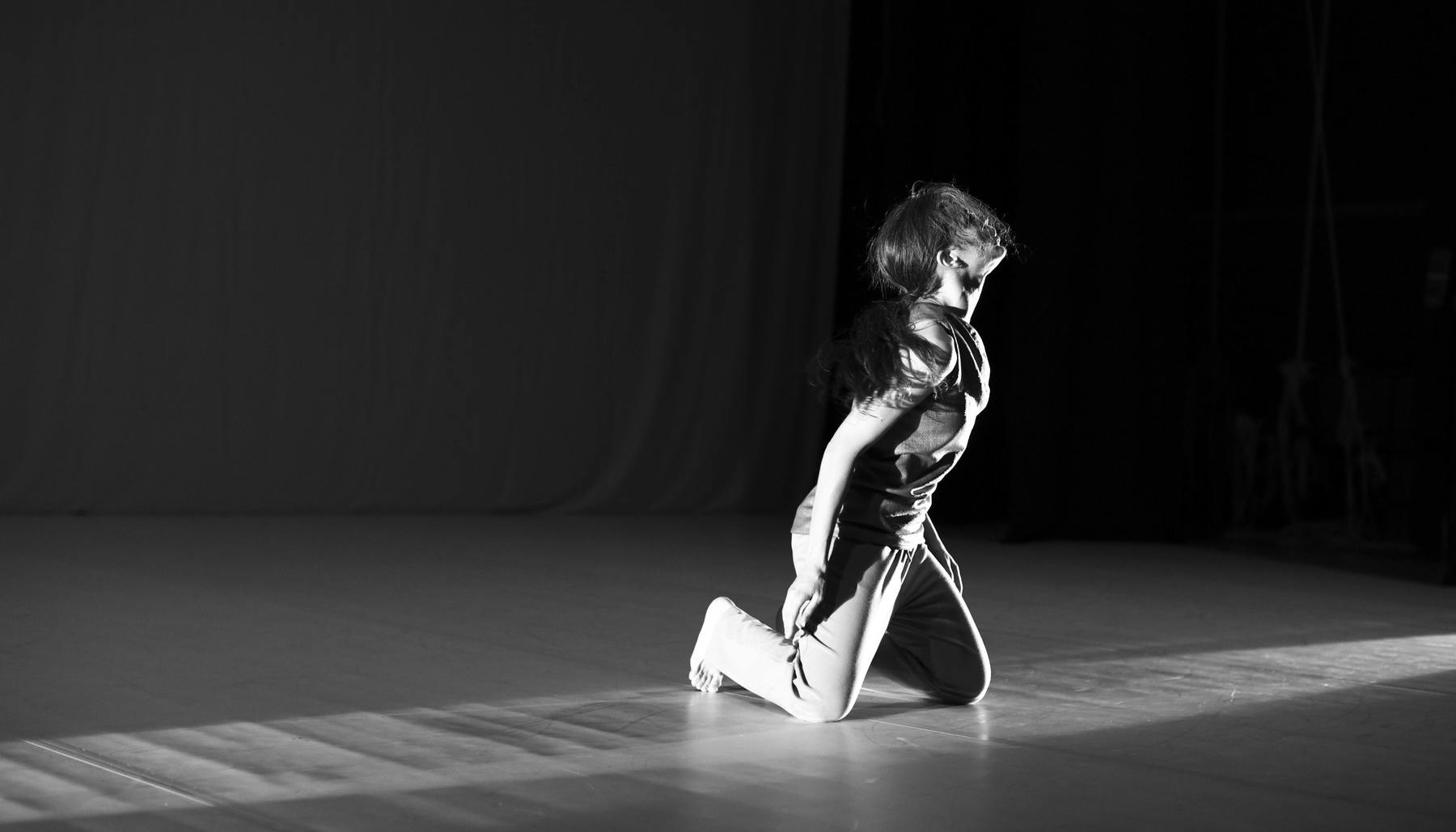 Black and white photo of kneeling performer looking to her left