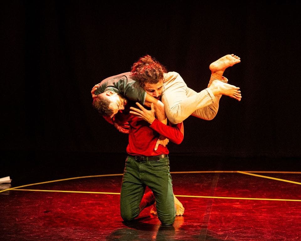 A kneeling performer carries a second performer on his shoulders