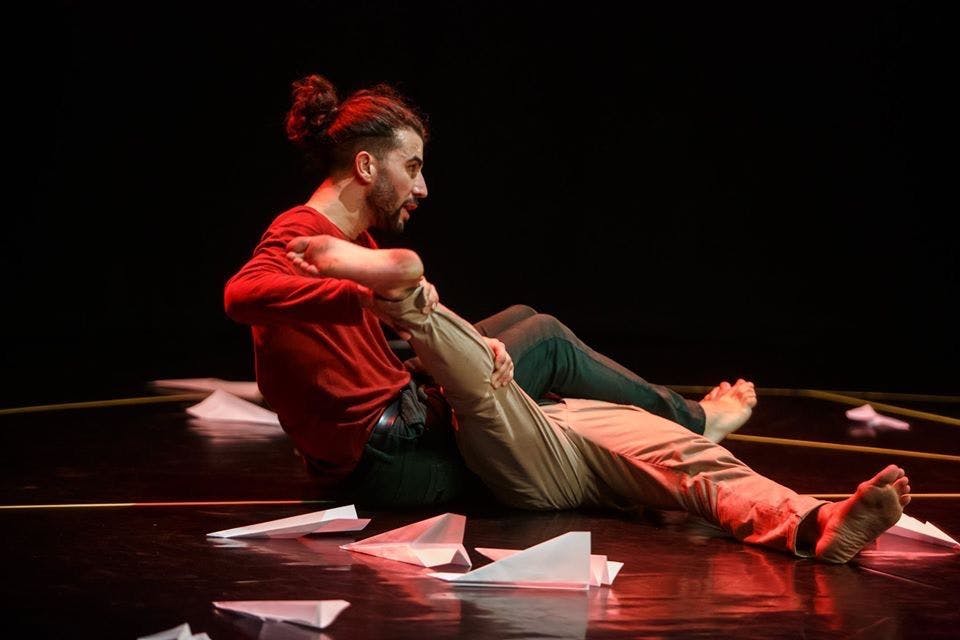 Un danzatore seduto sul palco tiene la gamba del secondo interprete sdraiato accanto a lui