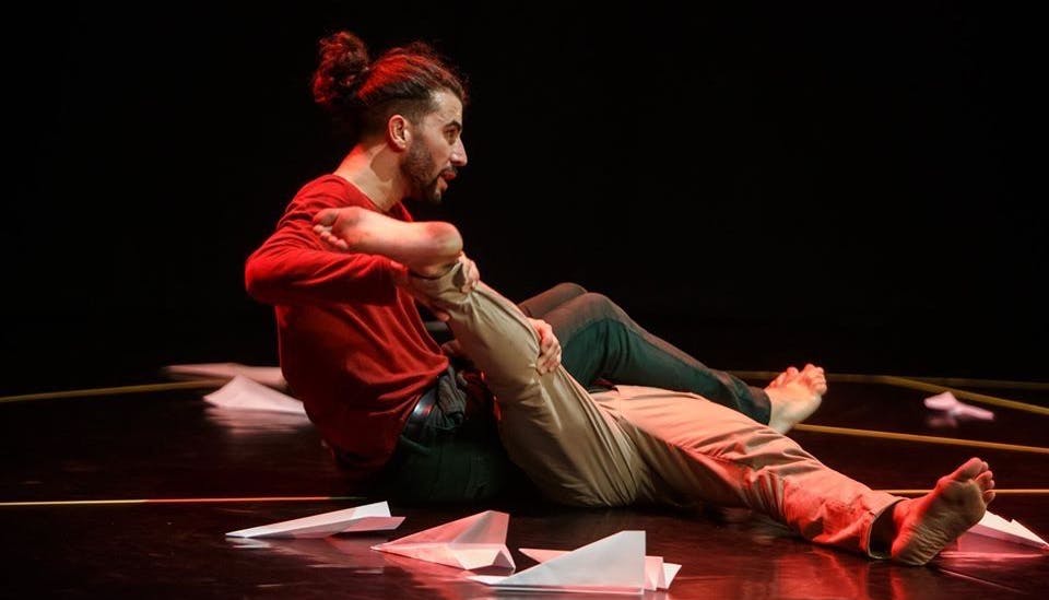 A dancer sitting on stage holds the leg of the second performer lying next to him