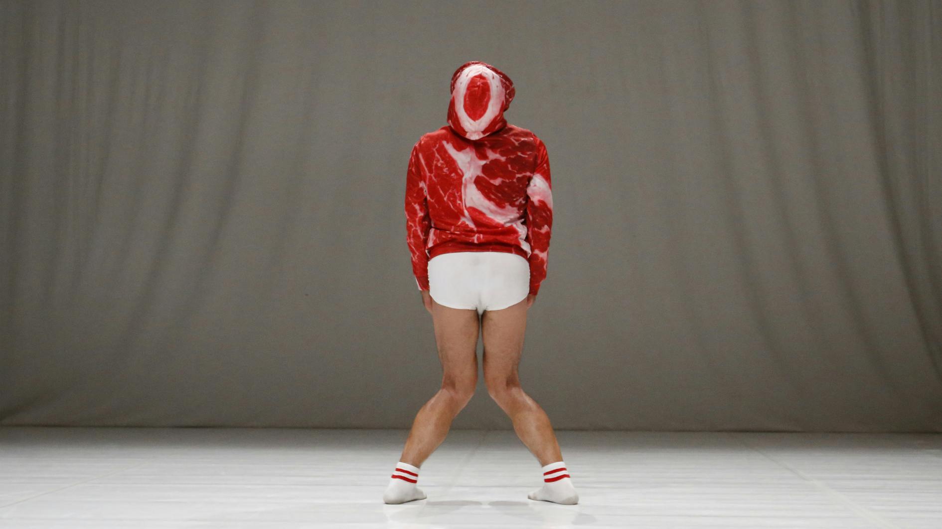 Dancer Carlo Massari in a pose with his knees close together turned towards the back of the room