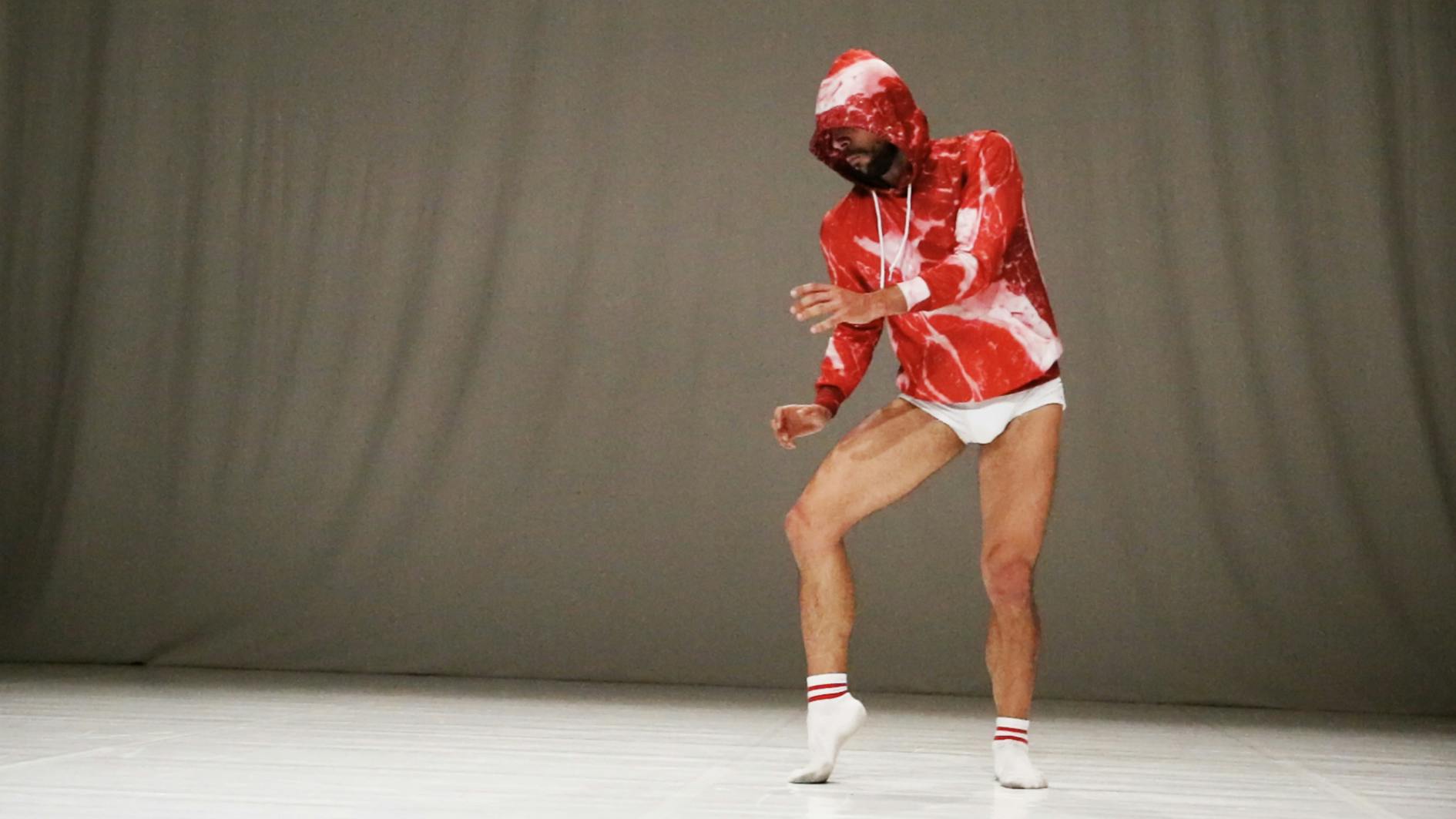 Dancer Carlo Massari posing in a red and white sweatshirt, the hood covers his face