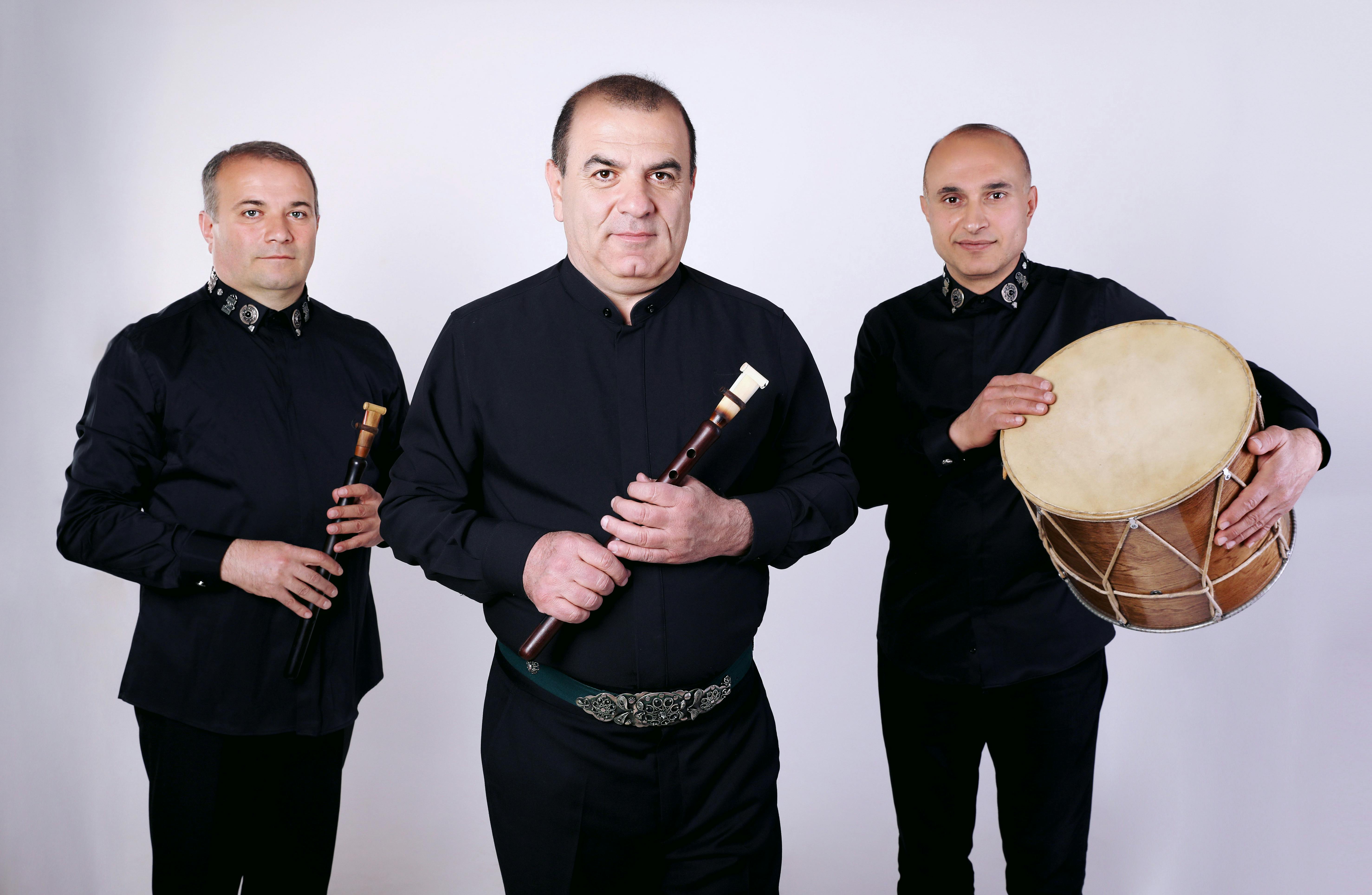 Gevorg Dabaghyan con ad altri due artisti vestiti di nero tengono in mano strumenti musicali tradizionali