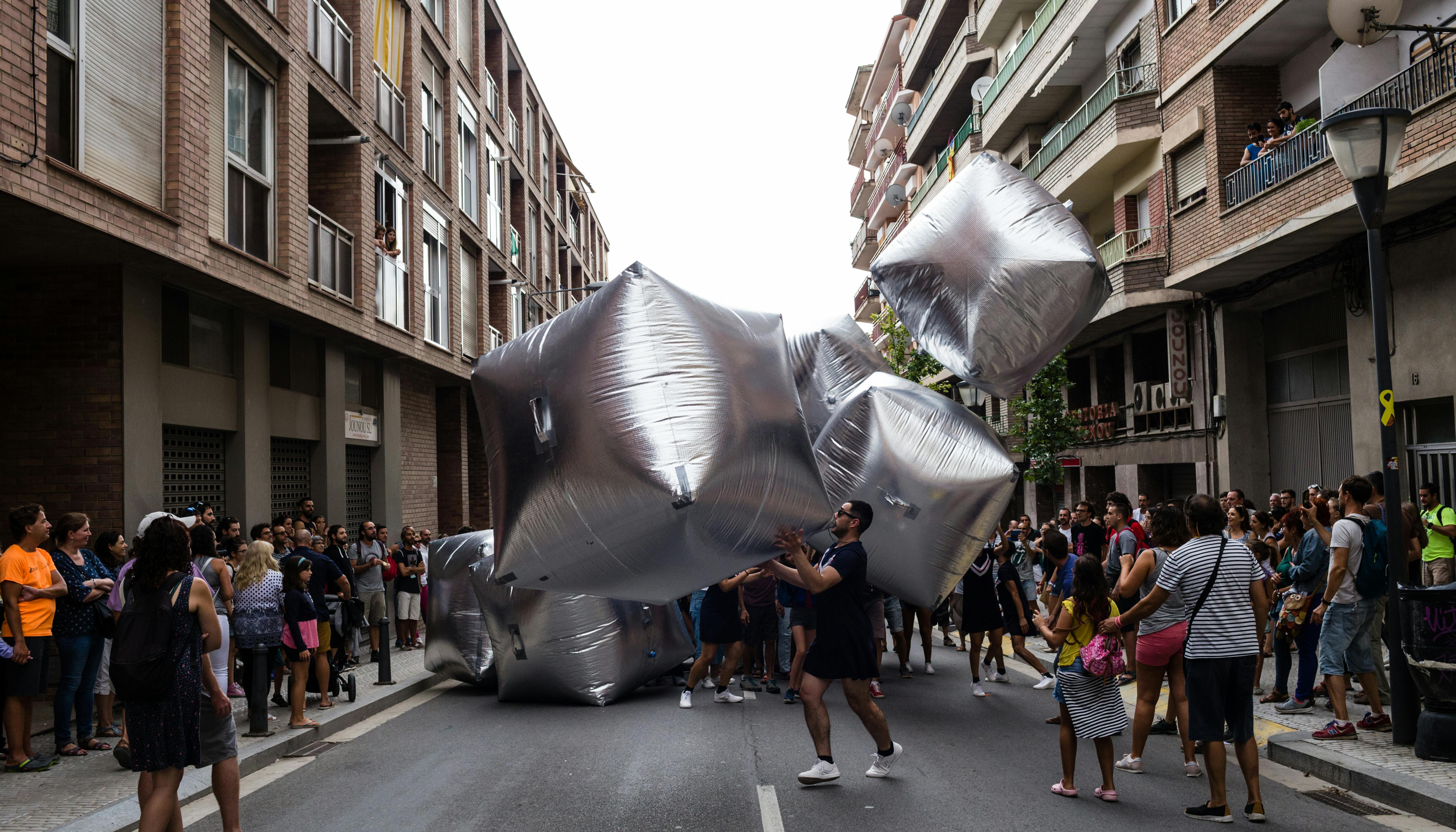 Dancers perform with inflatable silver cubes in the streets of the city
