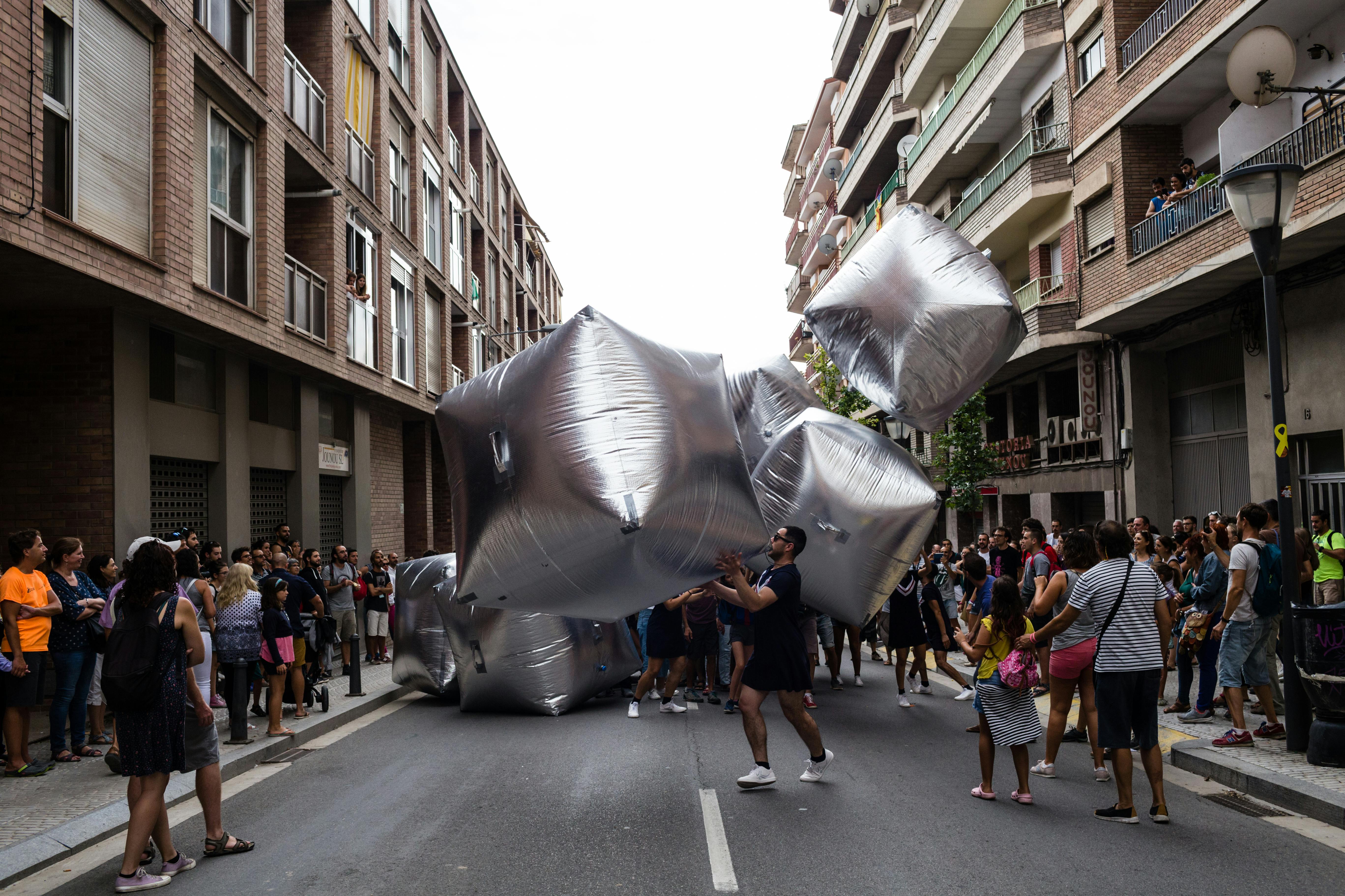 Dancers perform with inflatable silver cubes in the streets of the city