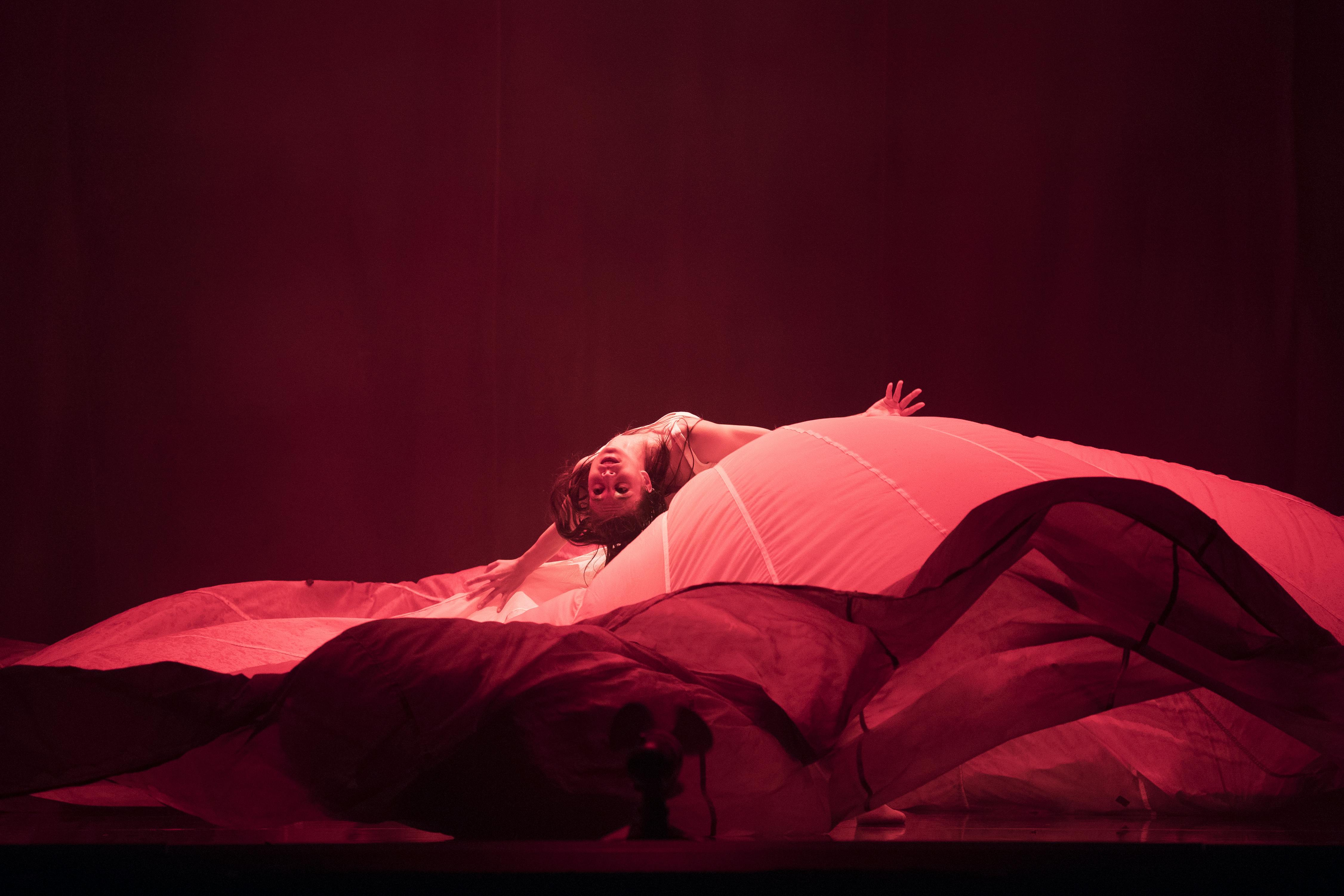 A dancer performs in one on stage wrapped in dark red cloth