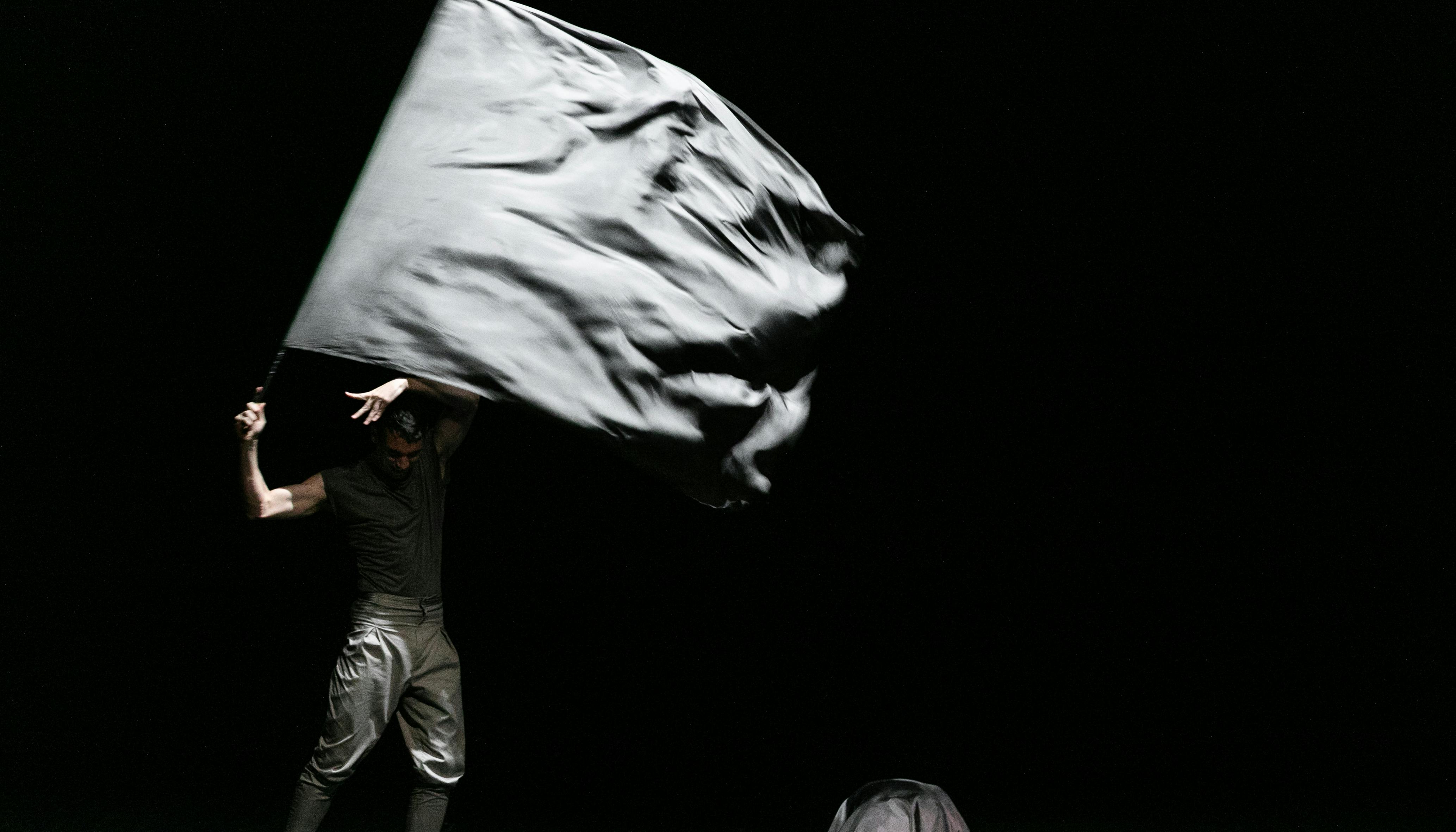 L'artista si esibisce sul palco indossando vestiti scuri e facendo sventolare una bandiera grigia