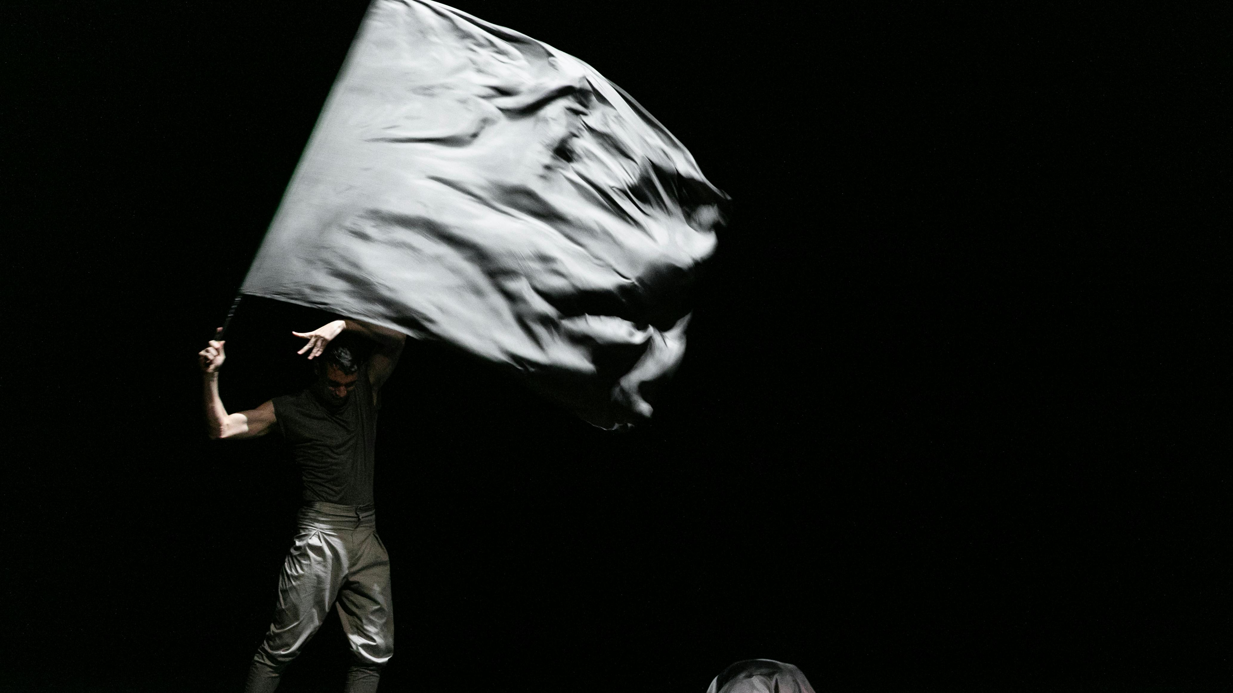 L'artista si esibisce sul palco indossando vestiti scuri e facendo sventolare una bandiera grigia