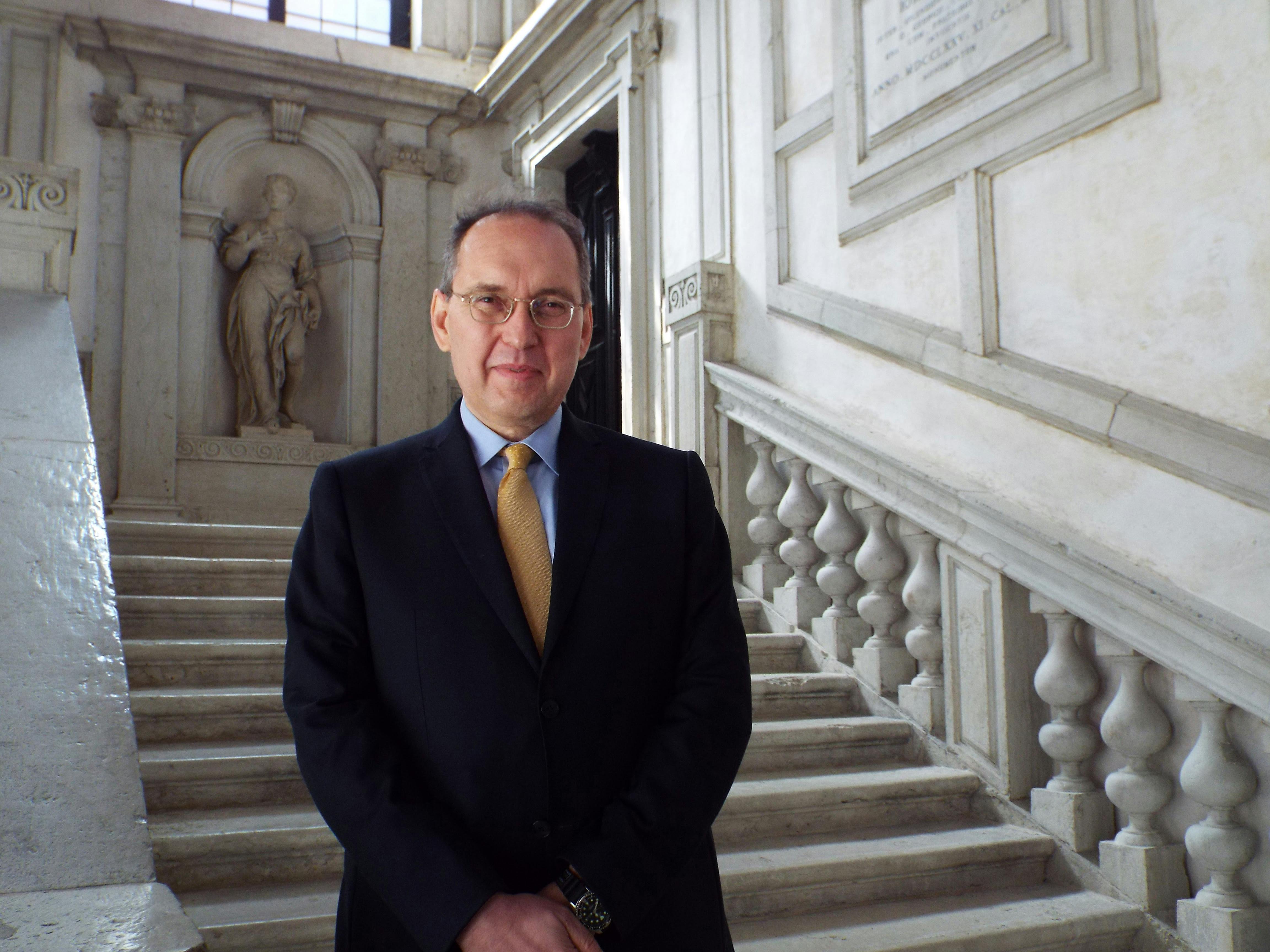 Egidio Ivetic sorridente con giacca e cravatta sulle scale di un palazzo storico
