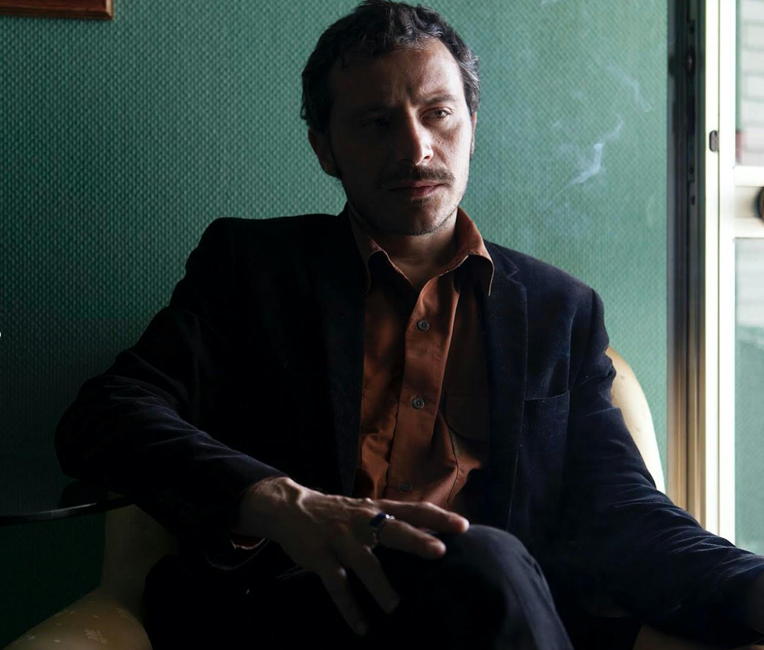 Marcello Anselmo seduto su una poltrona con un completo scuro