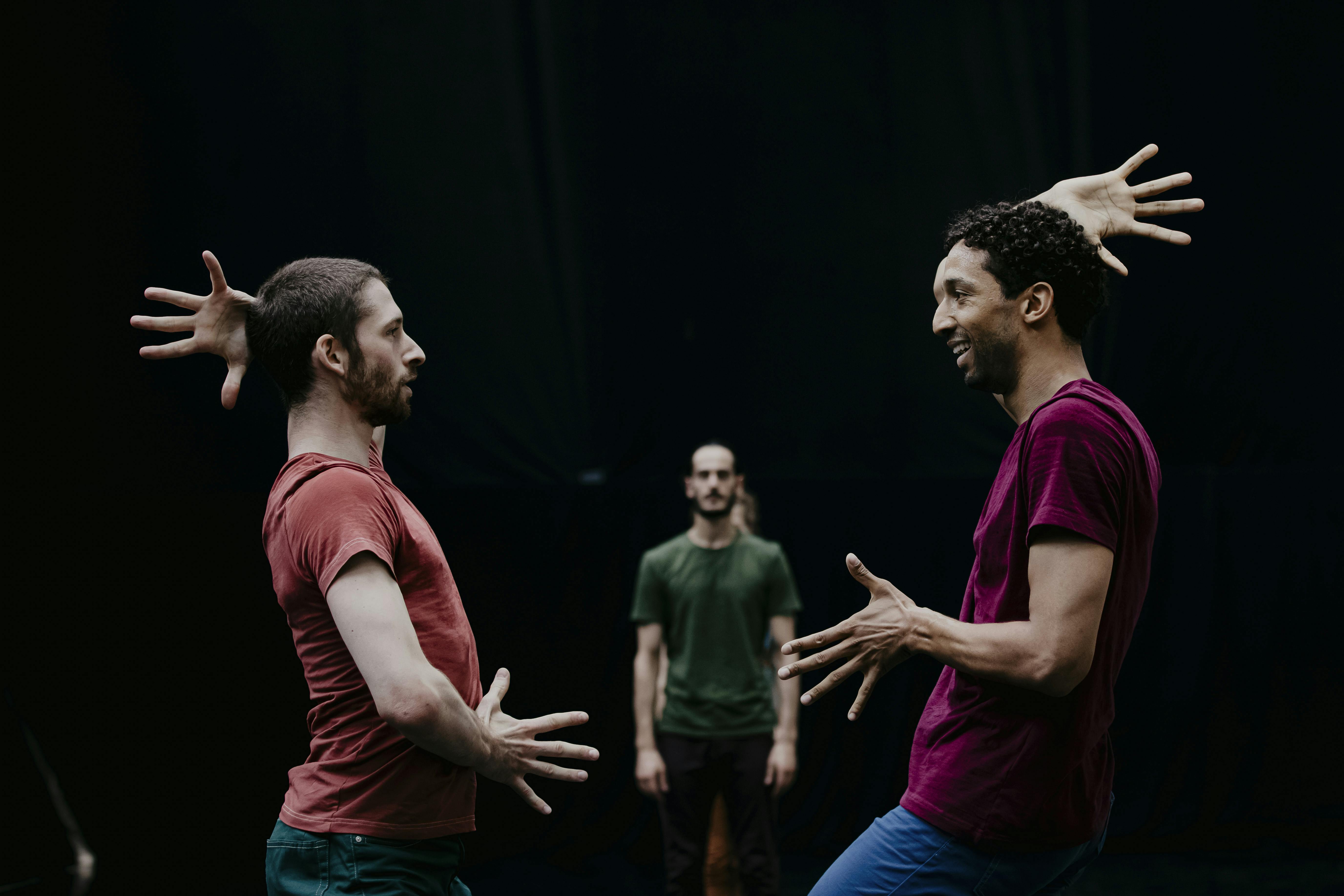 Philippe Kratz and another dancer facing each other with one hand at abdomen level and one on the head