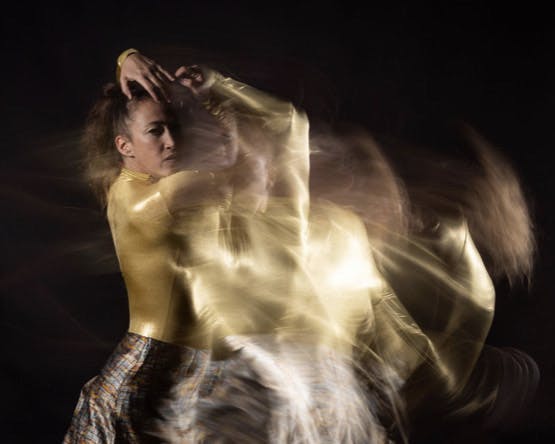 Adi Saloant wears a shiny gold leotard and the photograph has a movement effect 