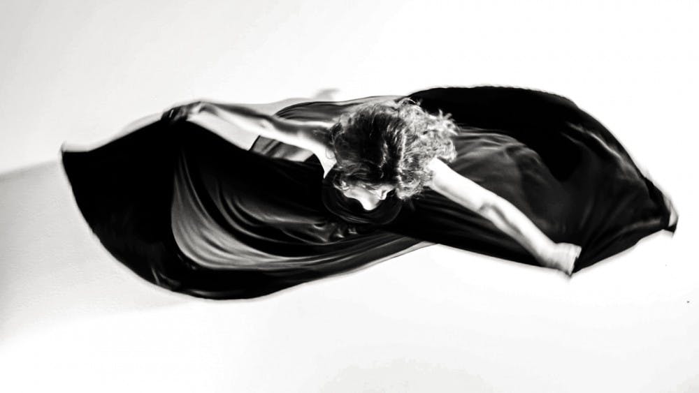 Silvia Perrone in a black and white top-down photo turns holding her dress with her arms raised