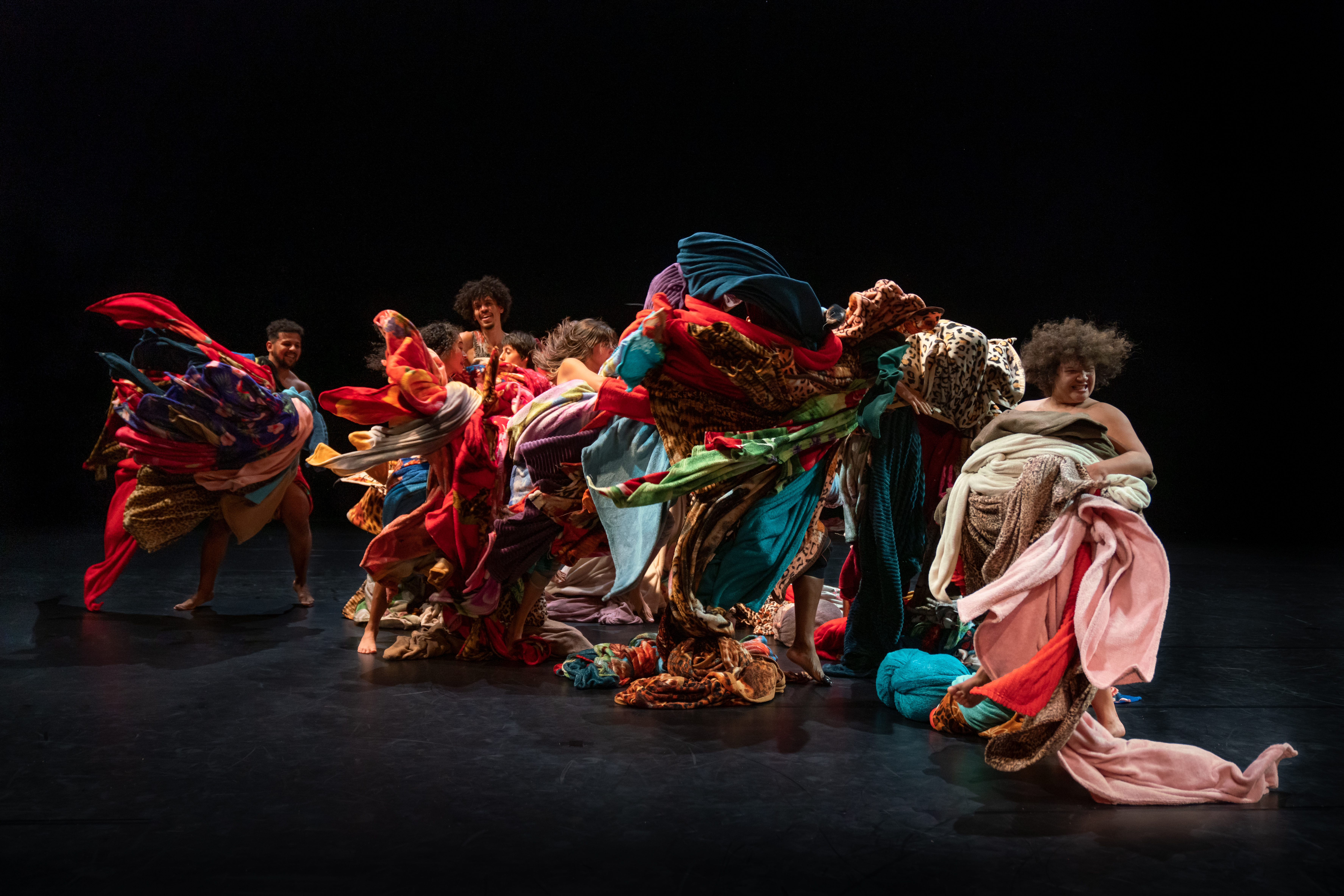 Dancers on a dark background wrapped in many coloured fabrics