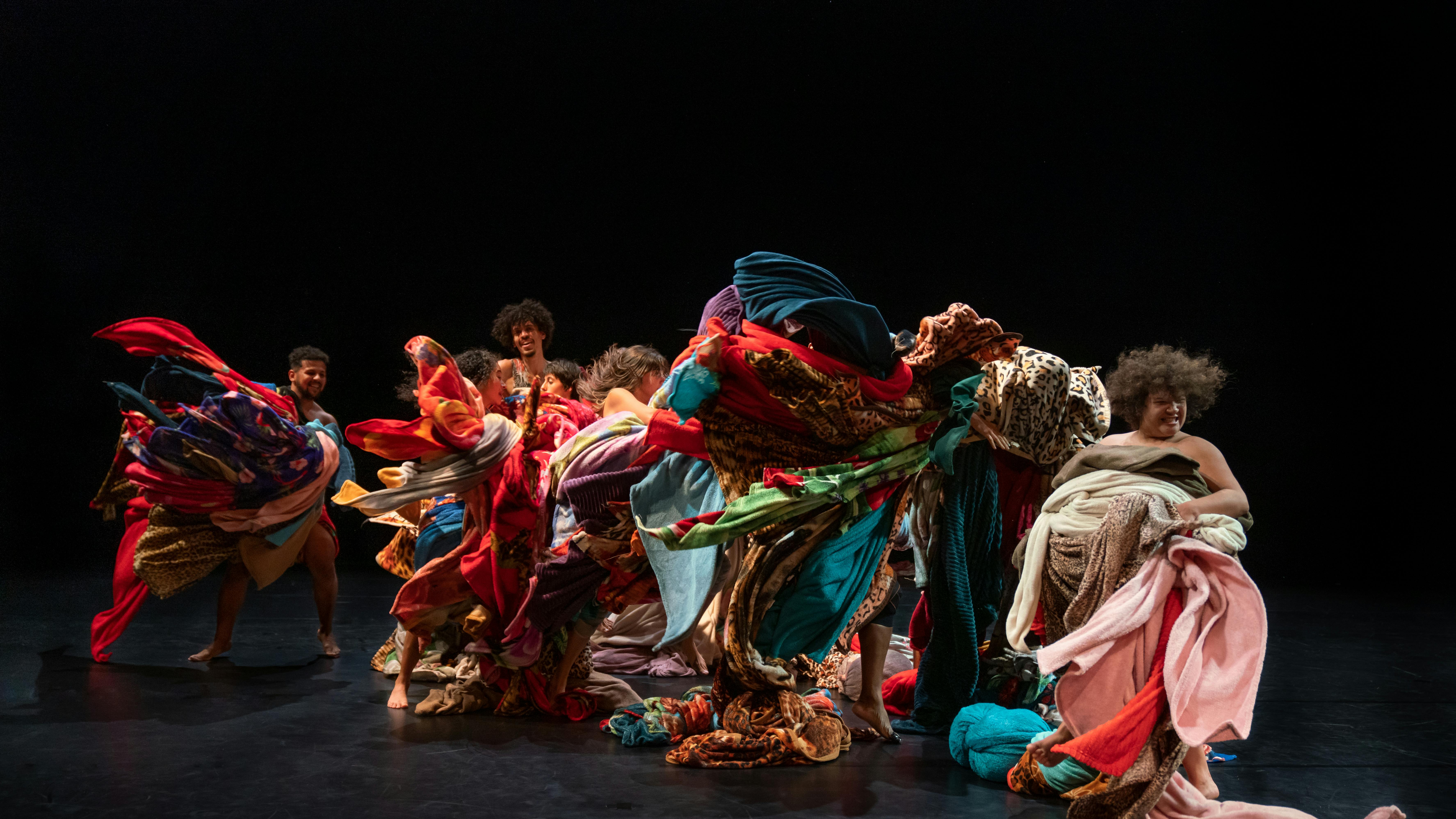 Dancers on a dark background wrapped in many coloured fabrics