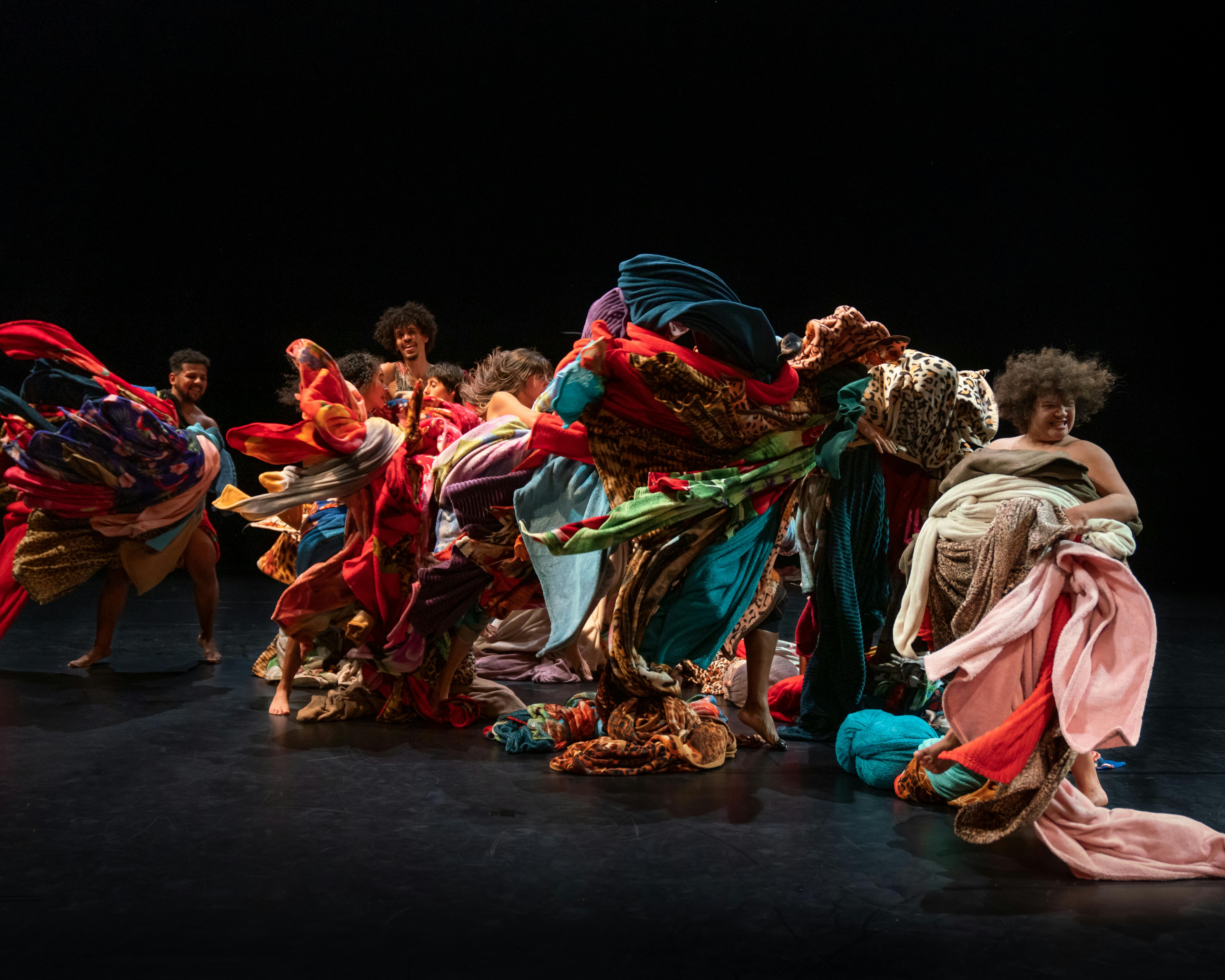 Dancers on a dark background wrapped in many coloured fabrics