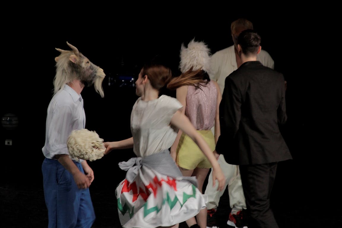 Danzatori in scena ed in movimento con vestiti ordinari e maschere di pecora sul volto 