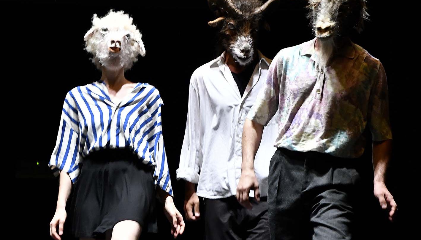 Three performers standing on stage wearing masks with animal heads 