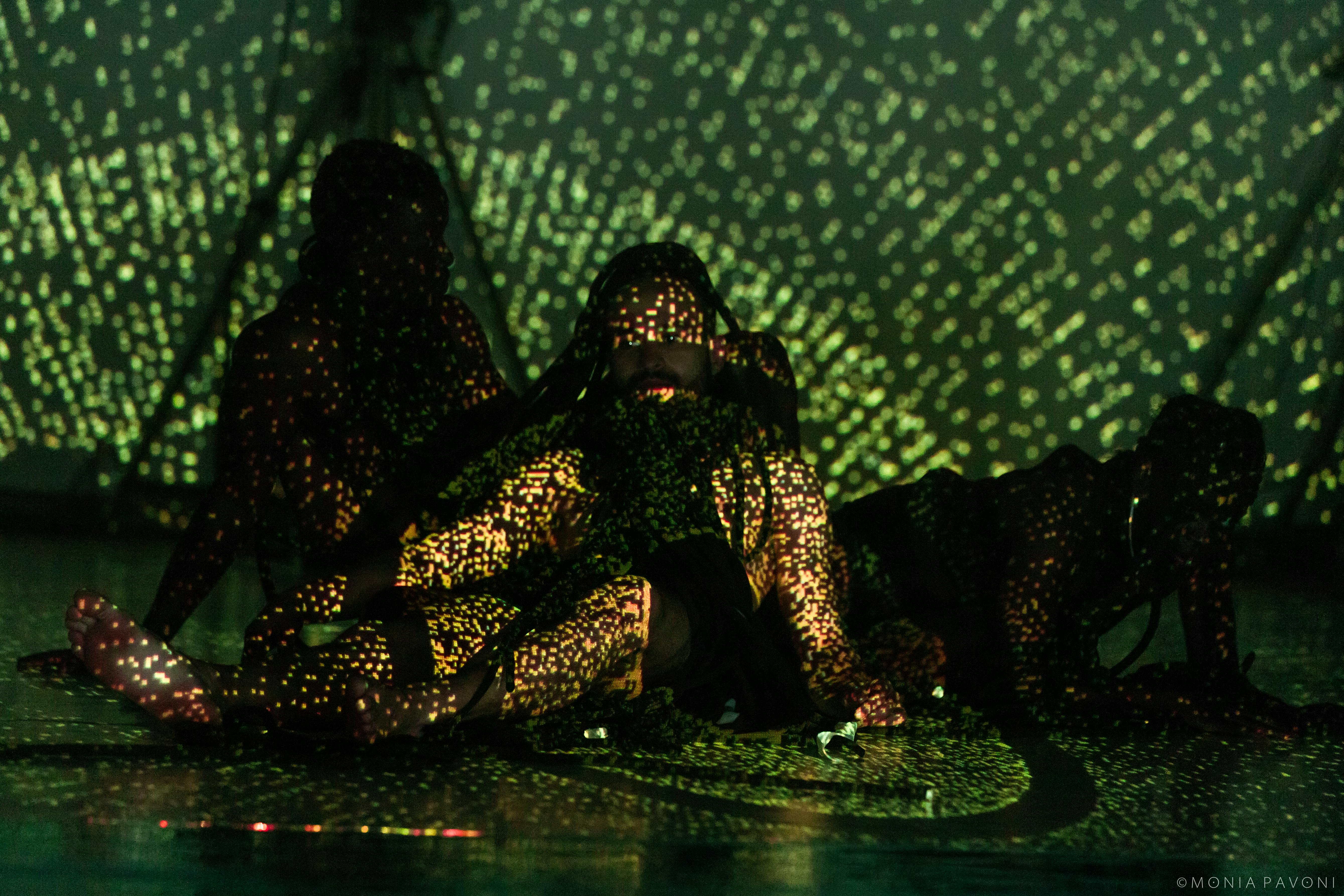 Three seated dancers illuminated by green and yellow lights