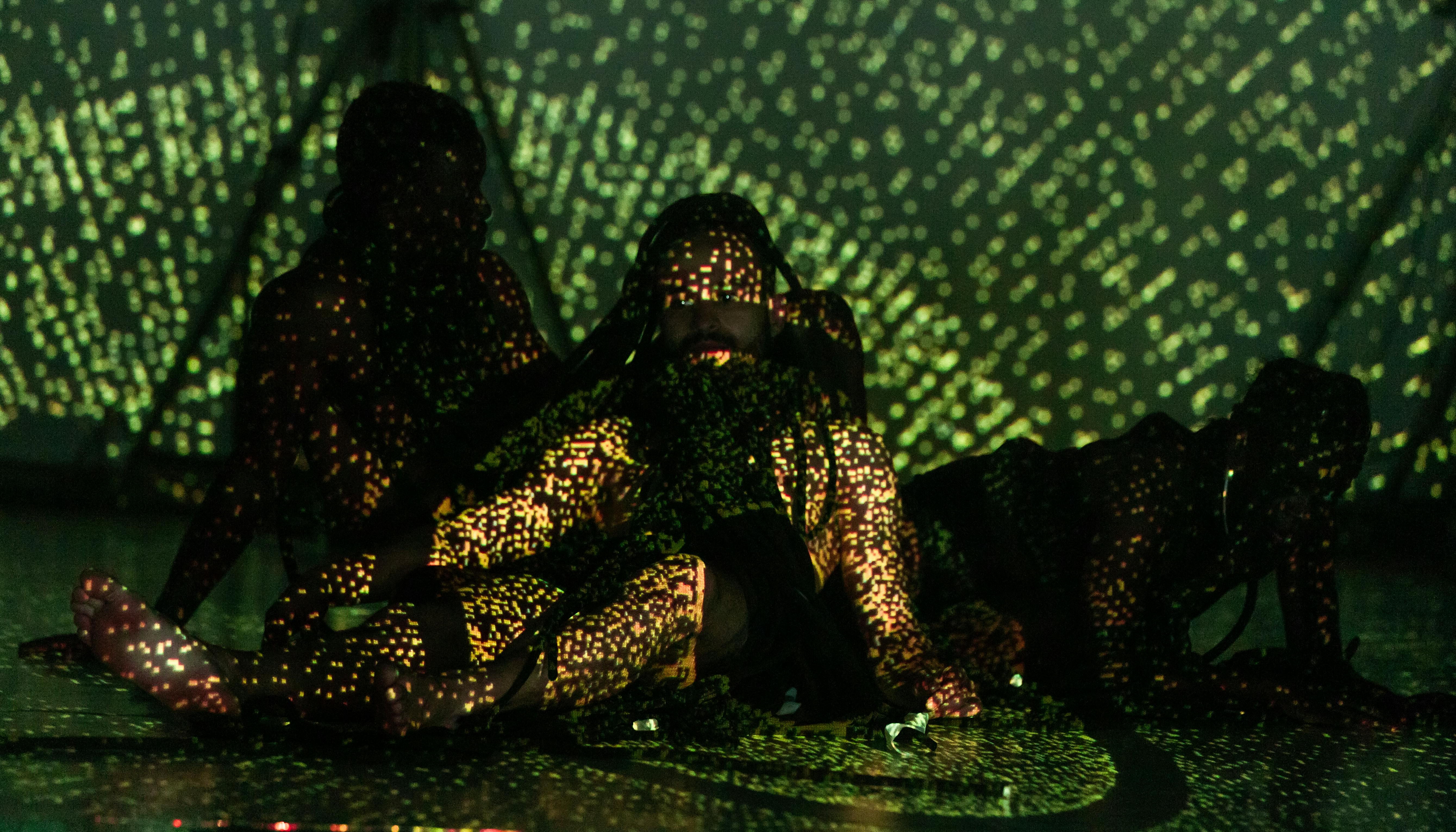Three seated dancers illuminated by green and yellow lights