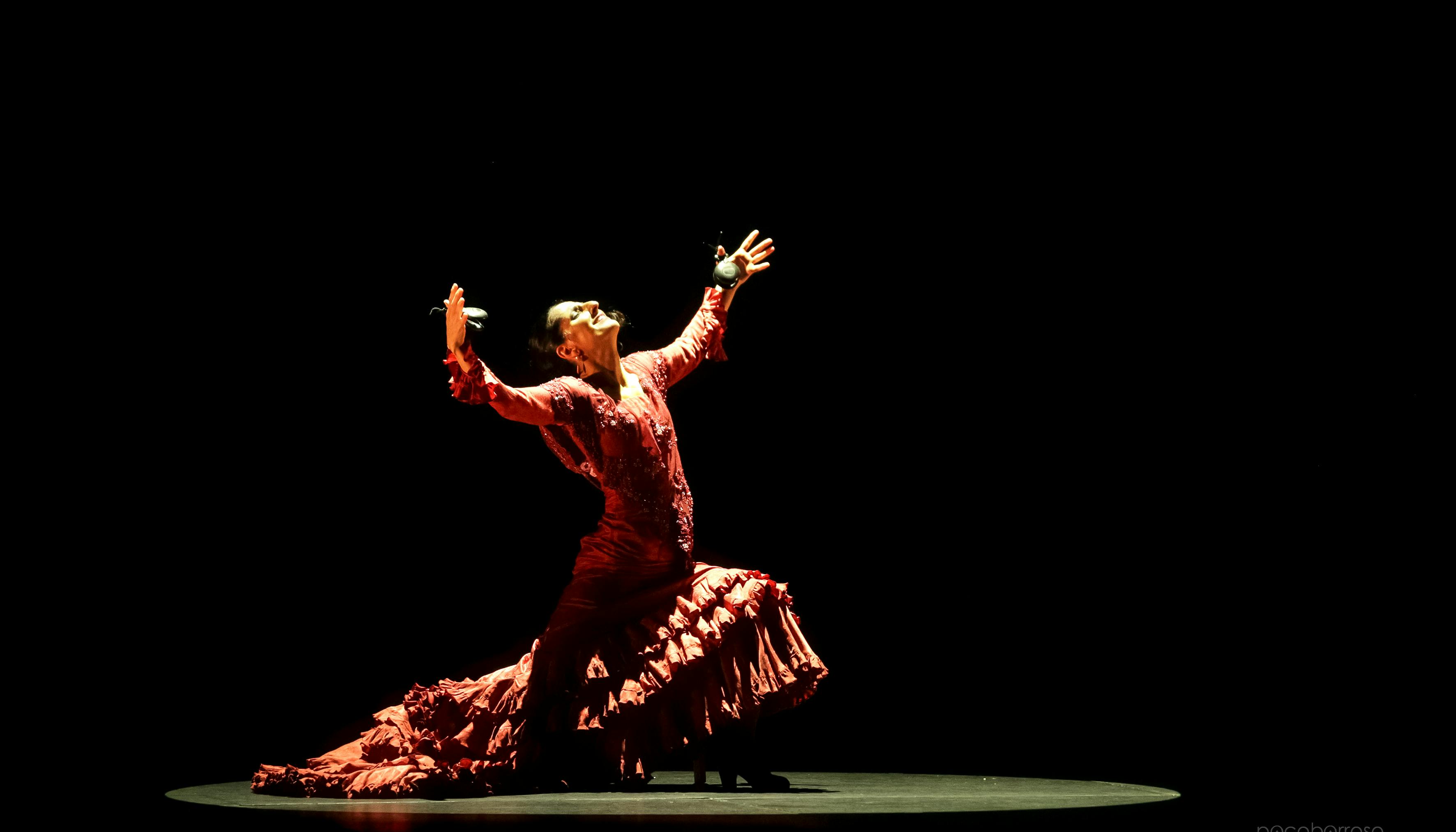 Mercedes Ruiz on stage with castanets in hand in an upwardly open position
