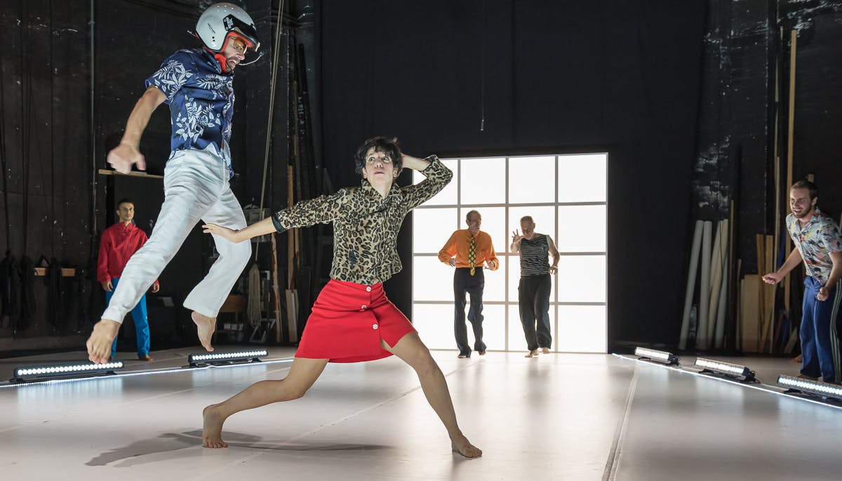 Danzatrice con gonna rossa al centro della foto un interprete esegue un salto alla sua destra