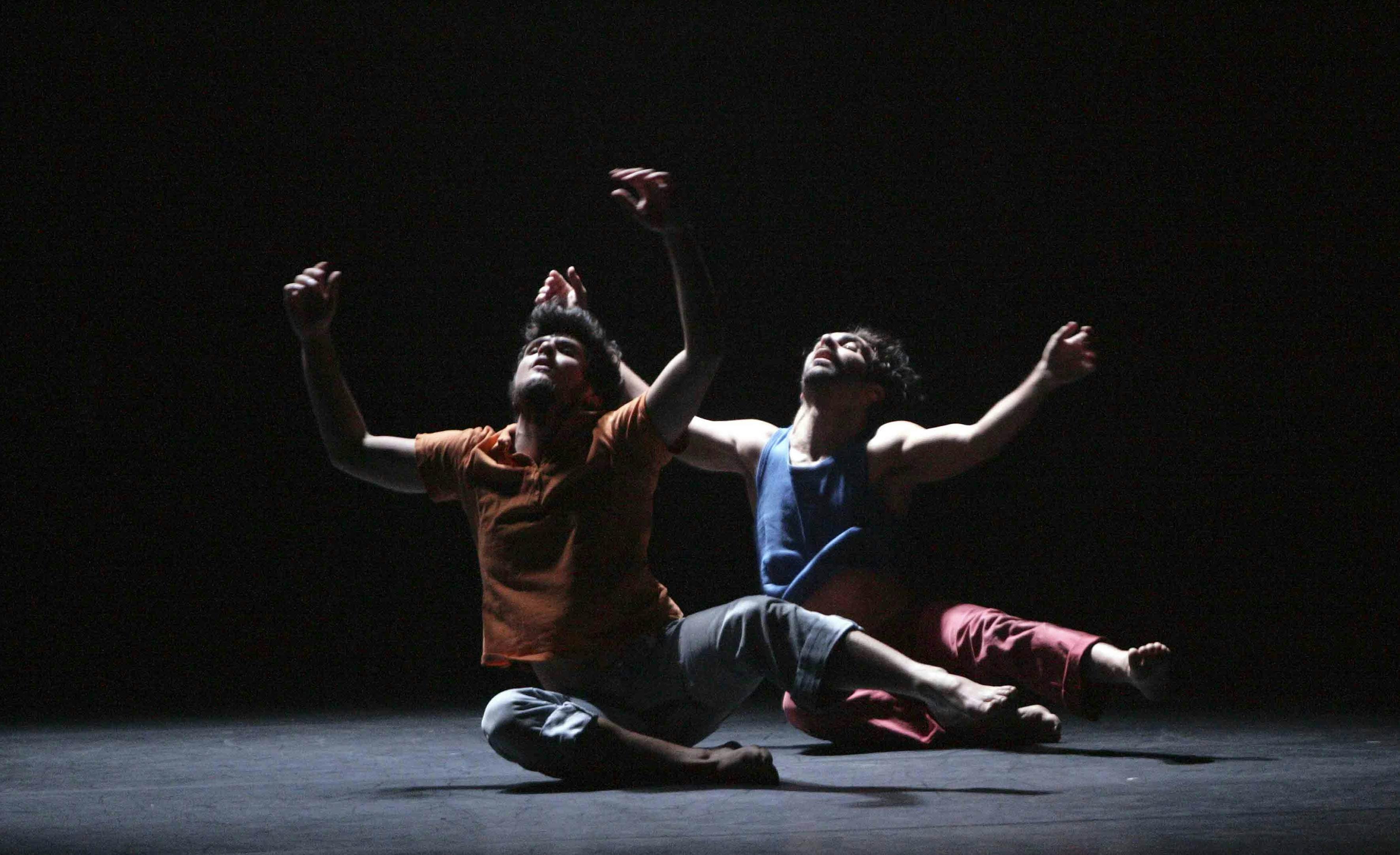 Two dancers seated on the floor with their arms and eyes pointing upwards