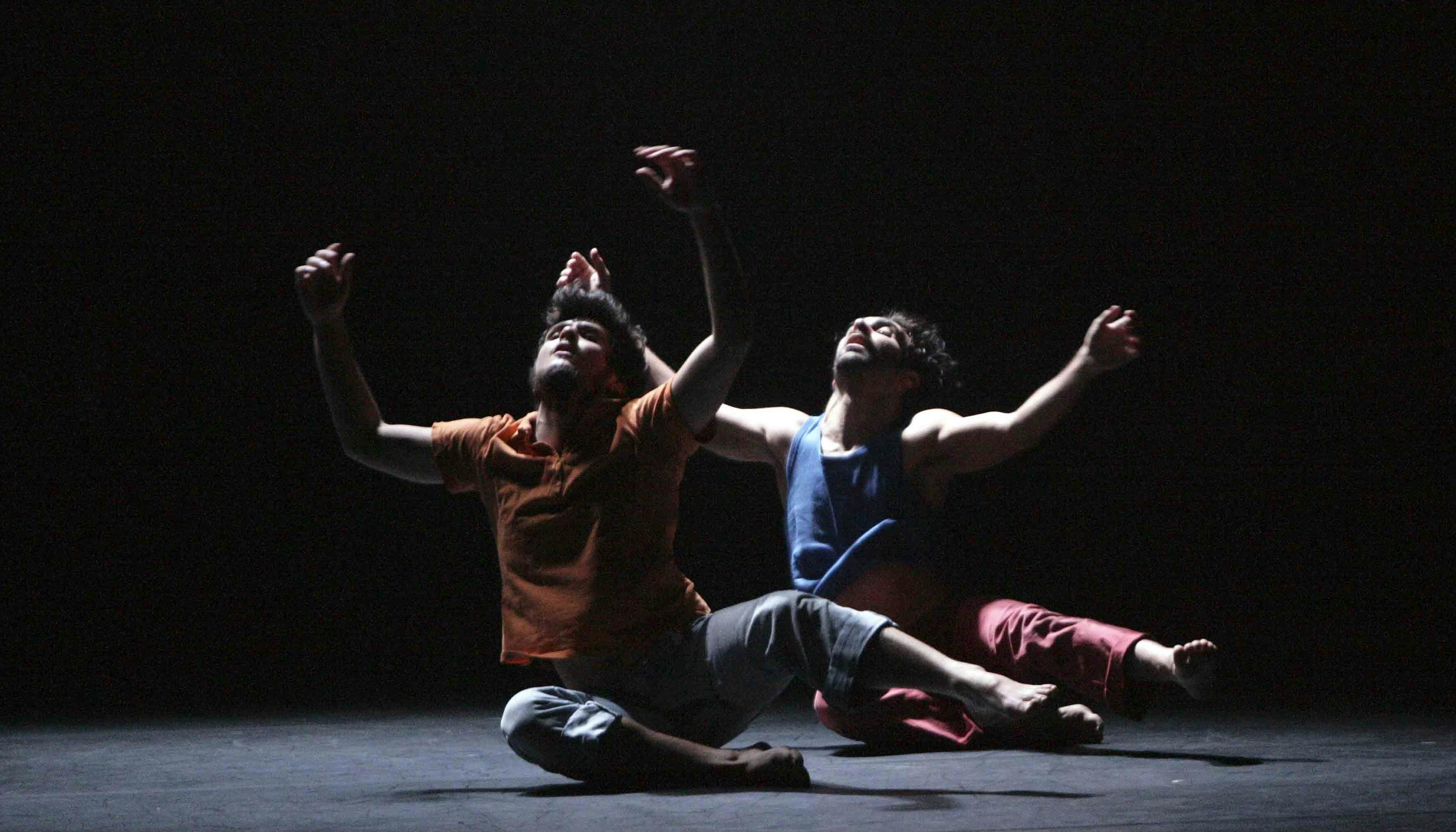 Two dancers seated on the floor with their arms and eyes pointing upwards