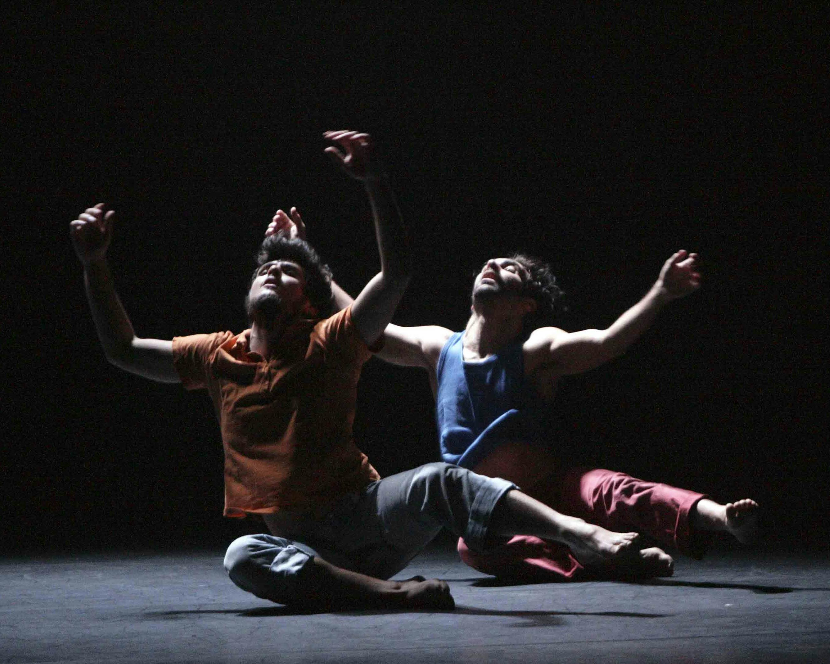 Due danzatori sono seduti sul pavimento con le braccia e lo sguardo rivolti verso l'alto
