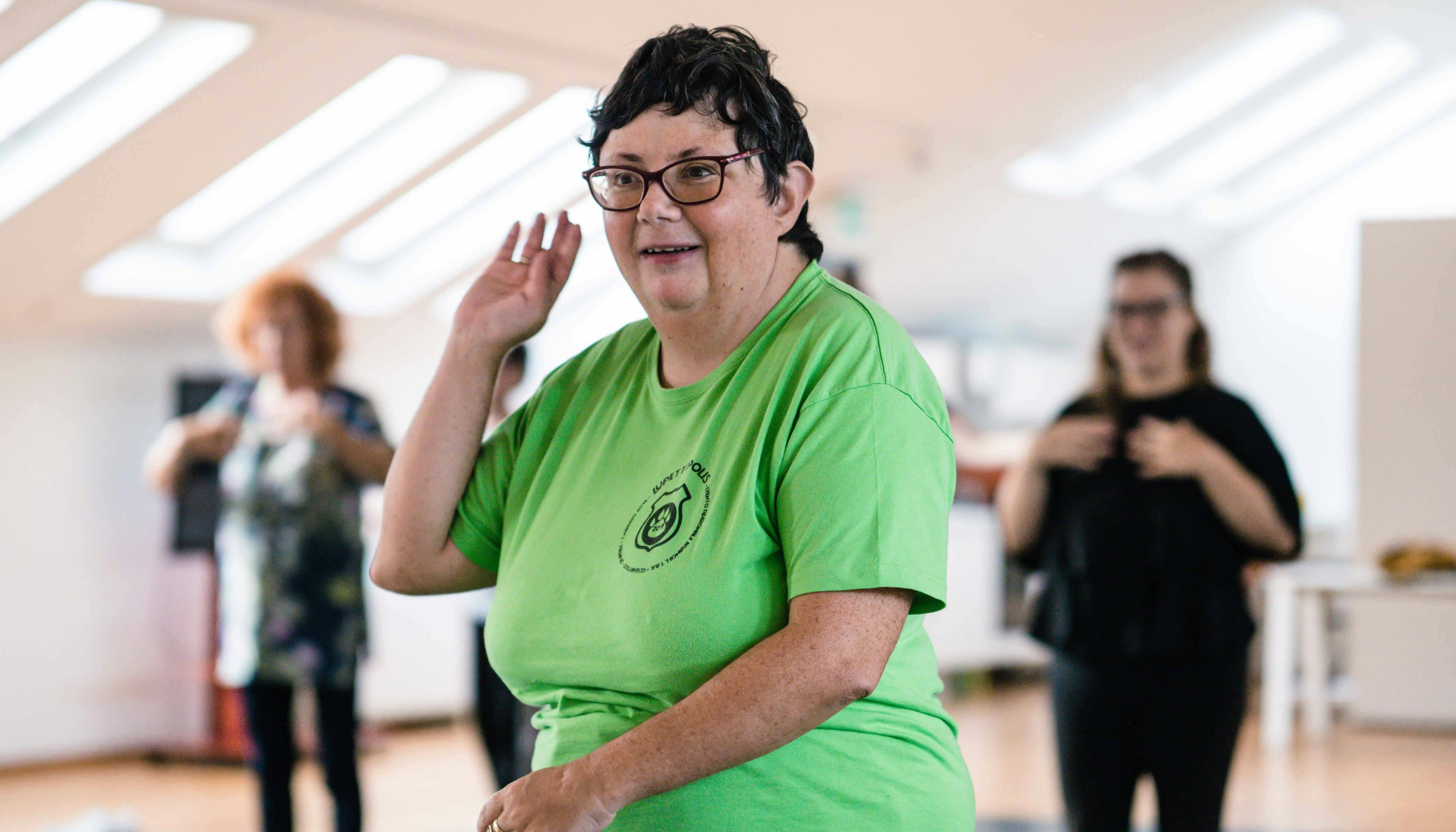 A participant in the session wears a green T-shirt and stretches her arm upwards