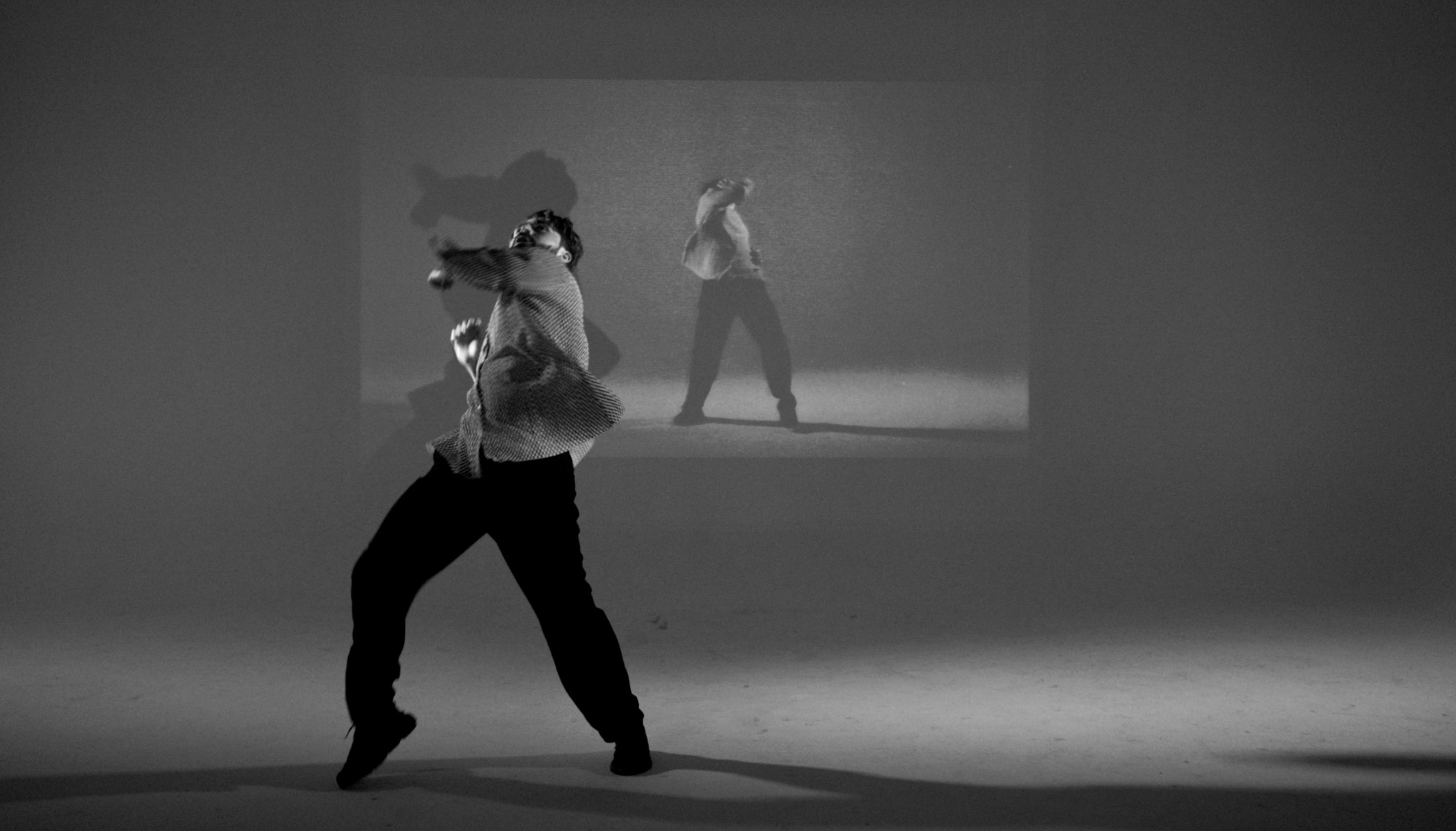 Simone Donati in una fotografia in bianco e nero in piedi alza il gomito in avanti