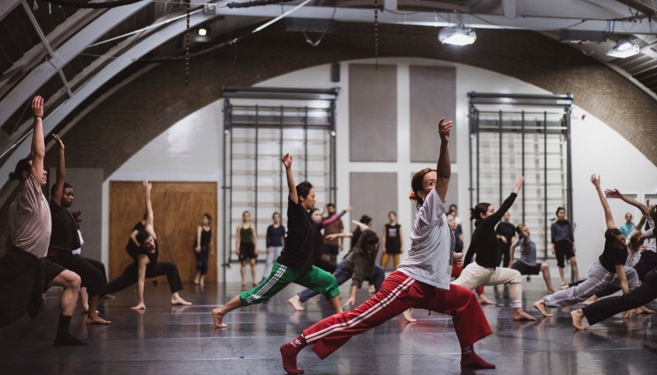 Dancers in the hall in a position with the right arm extended upwards, the left leg in plié and the right leg extended