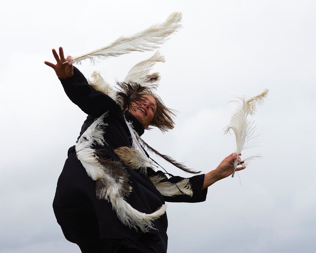 L'artista Kirstie Simson in movimento con delle piume sul vestito e in mano