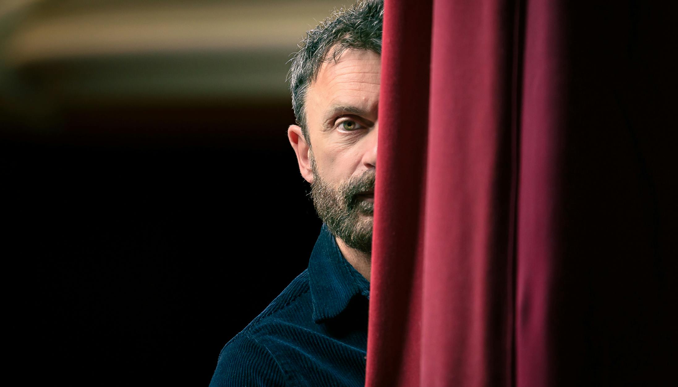 Close-up portrait of Emilio Calcagno half hidden by the red curtain