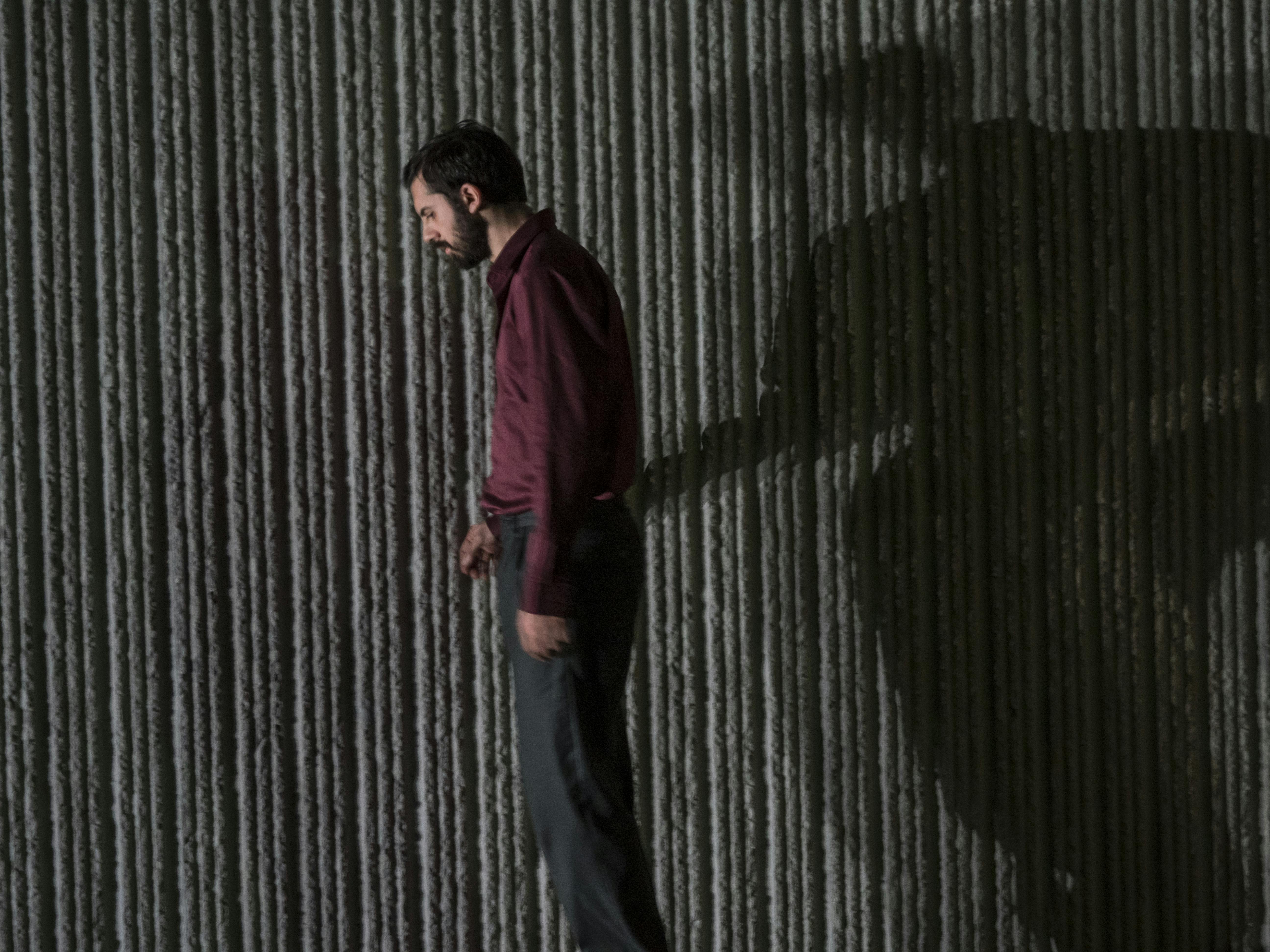 Alessio Maria Romano in piedi con una camicia bordeaux di profilo