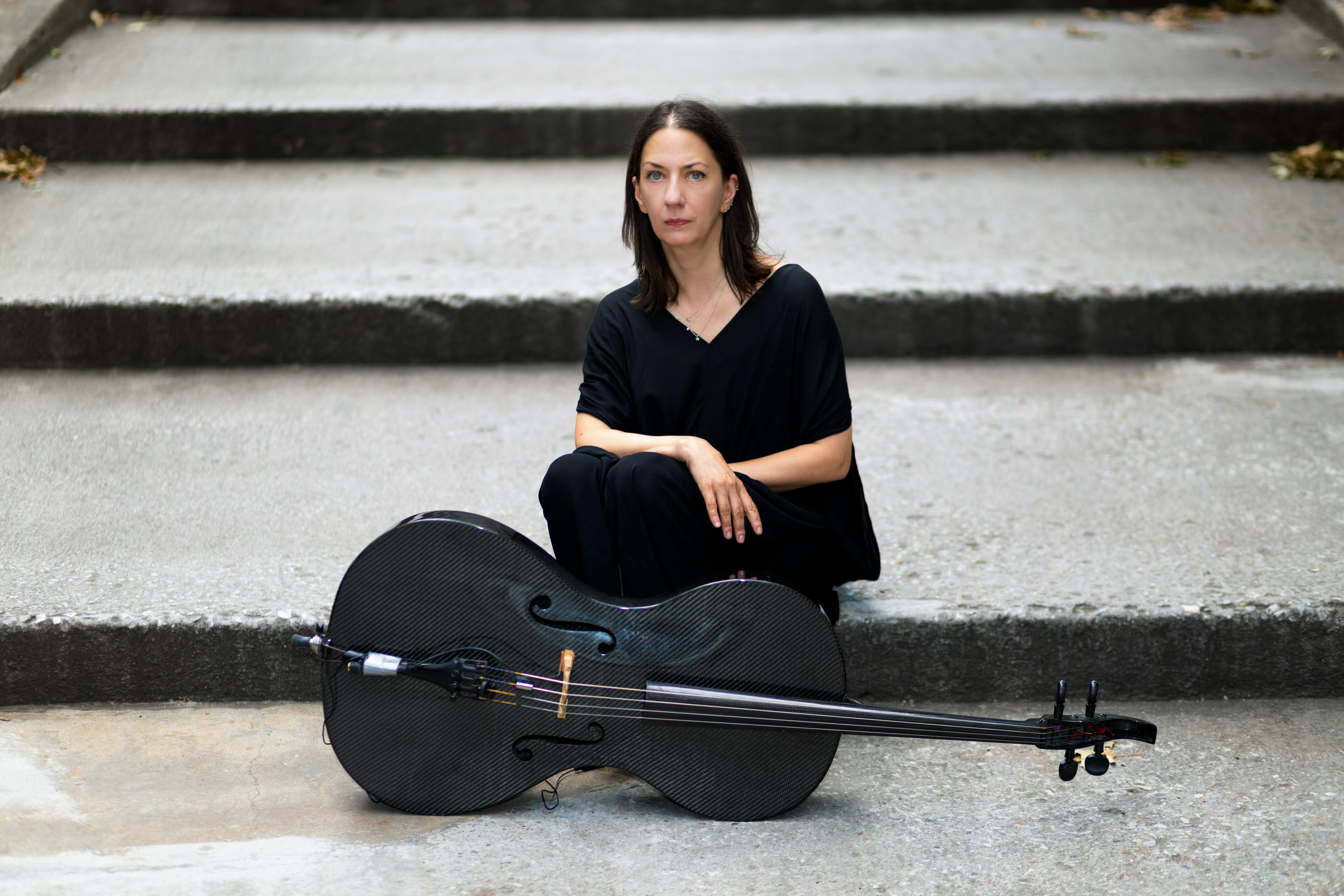 Julia Kent seduta su una scalinata vestita di nero con un violoncello davanti