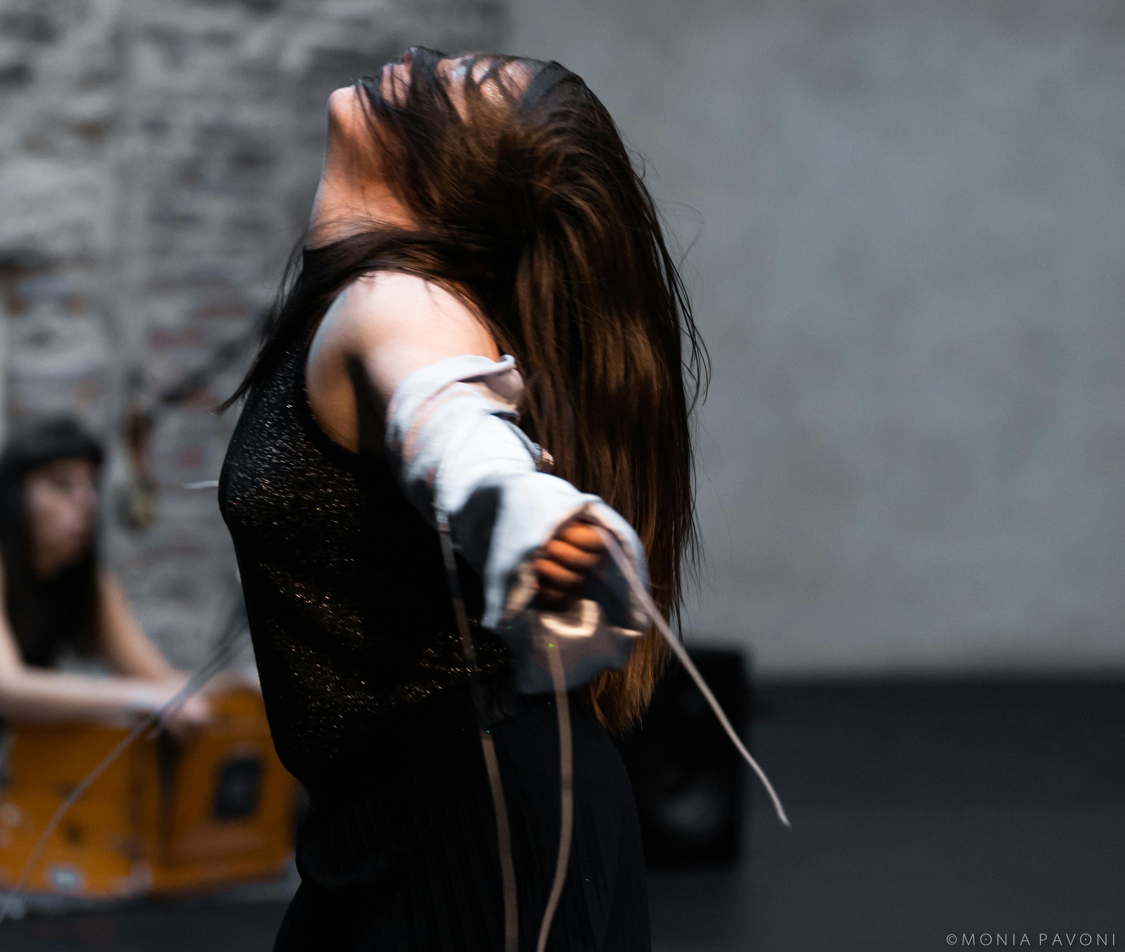 A dancer in profile looks upward with hair on her face.