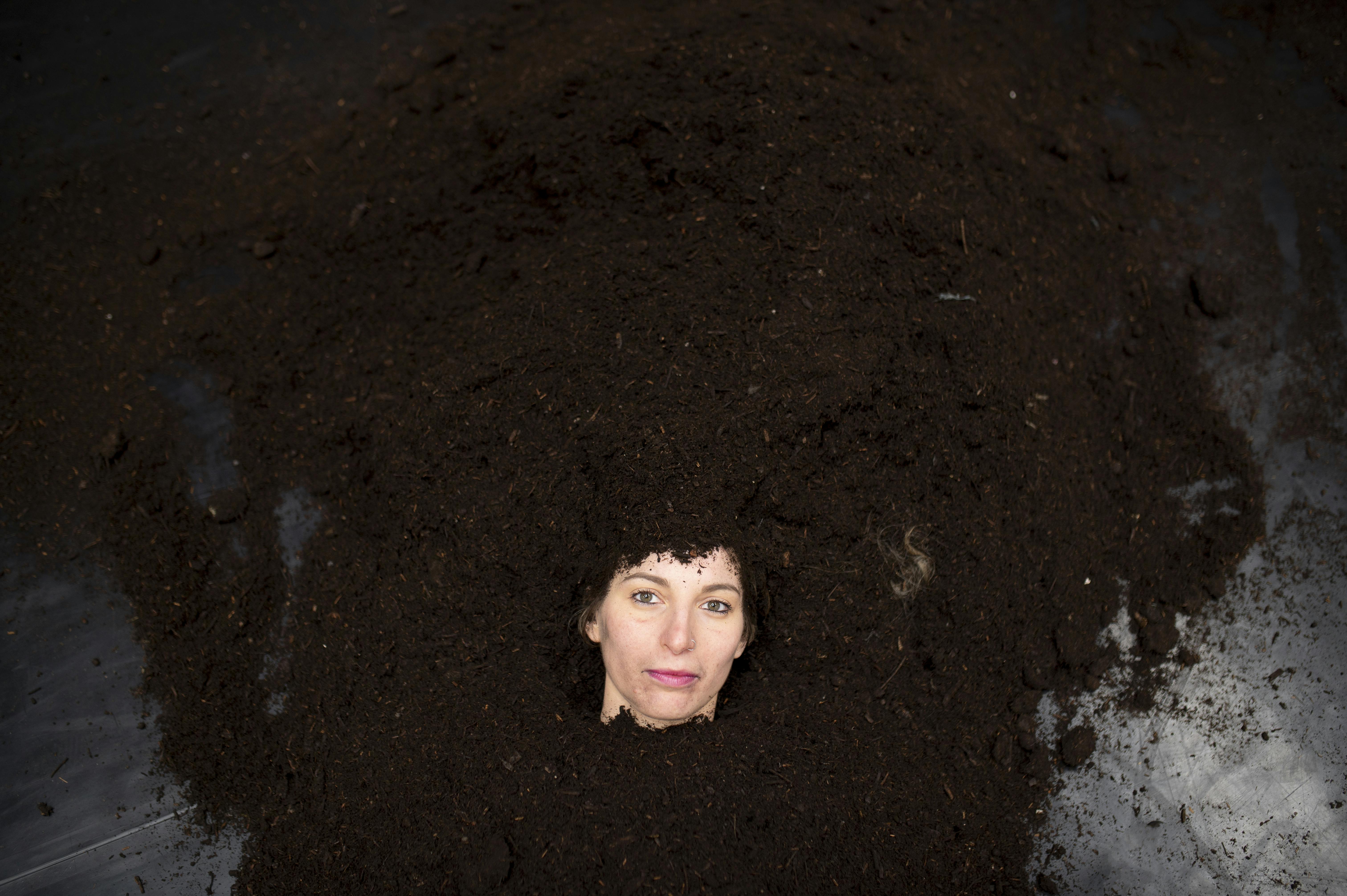 The face of the performer emerges from a pile of dirt spread on a dance mat