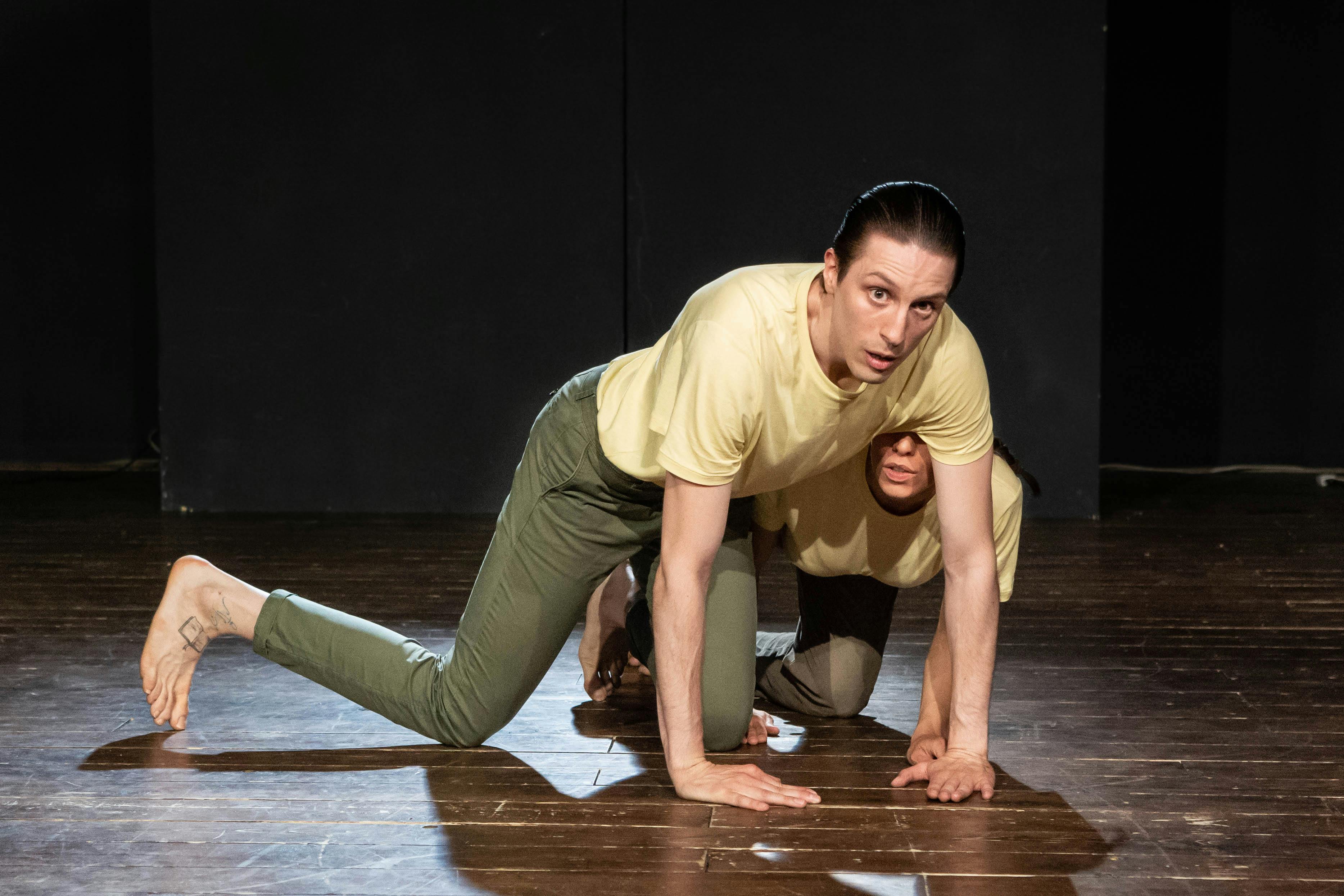 Two performers on stage the first on all fours and the second hides behind the dancer