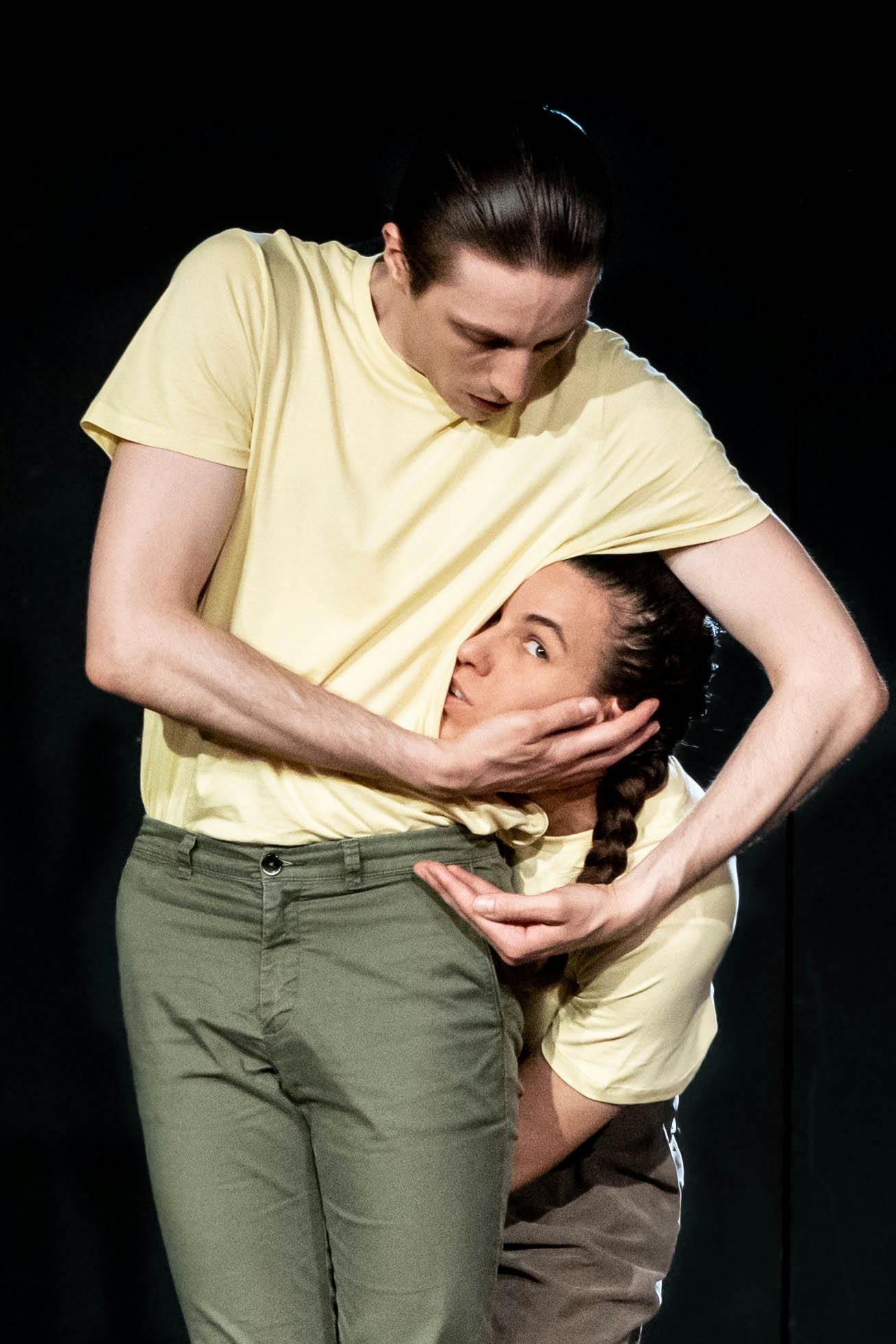 A standing dancer touches the face of a dancer who hides her face with the dancer's figure