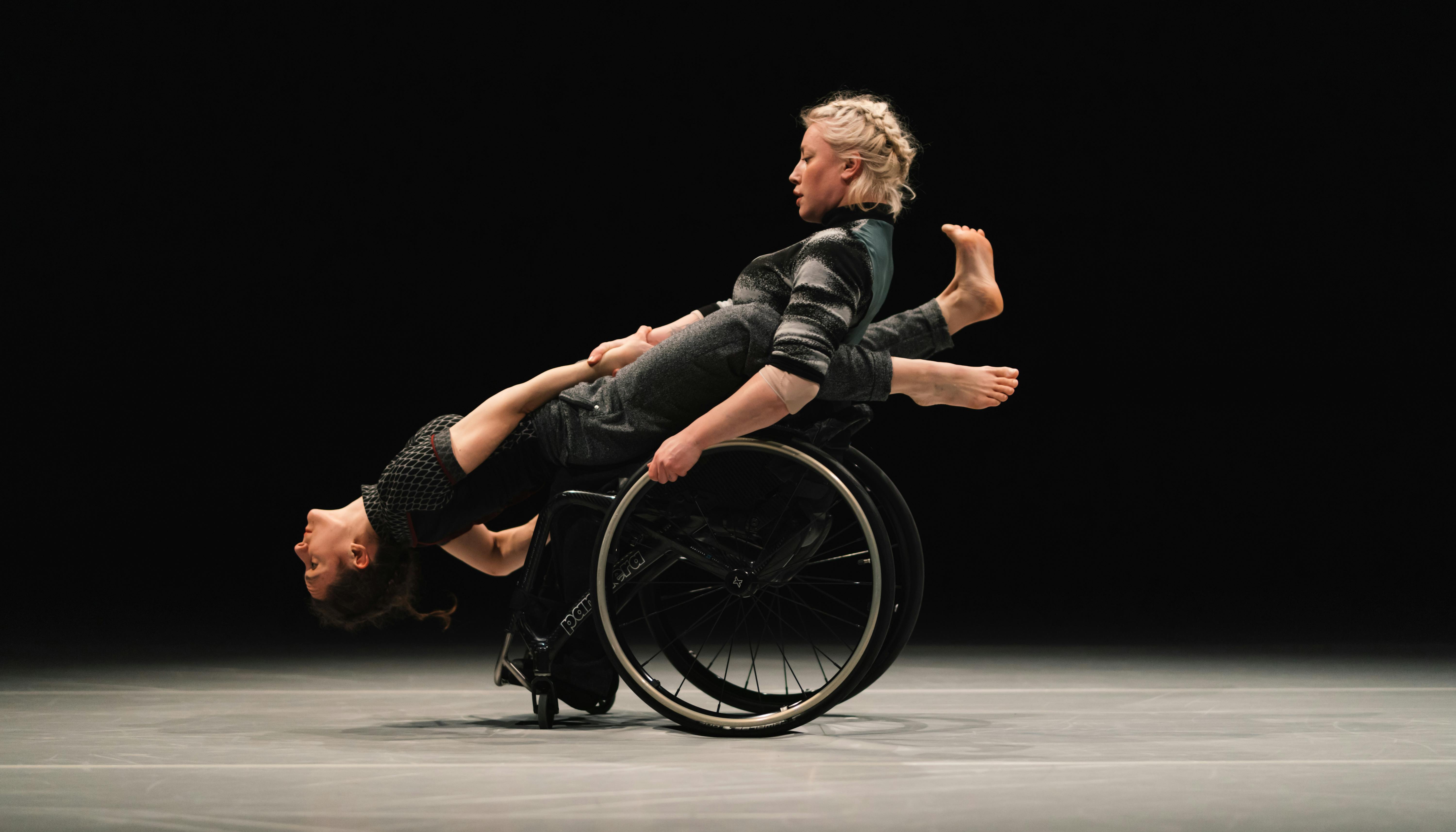 Una danzatrice con disabilità regge in equilibrio perpendicolare un'altra danzatrice.
