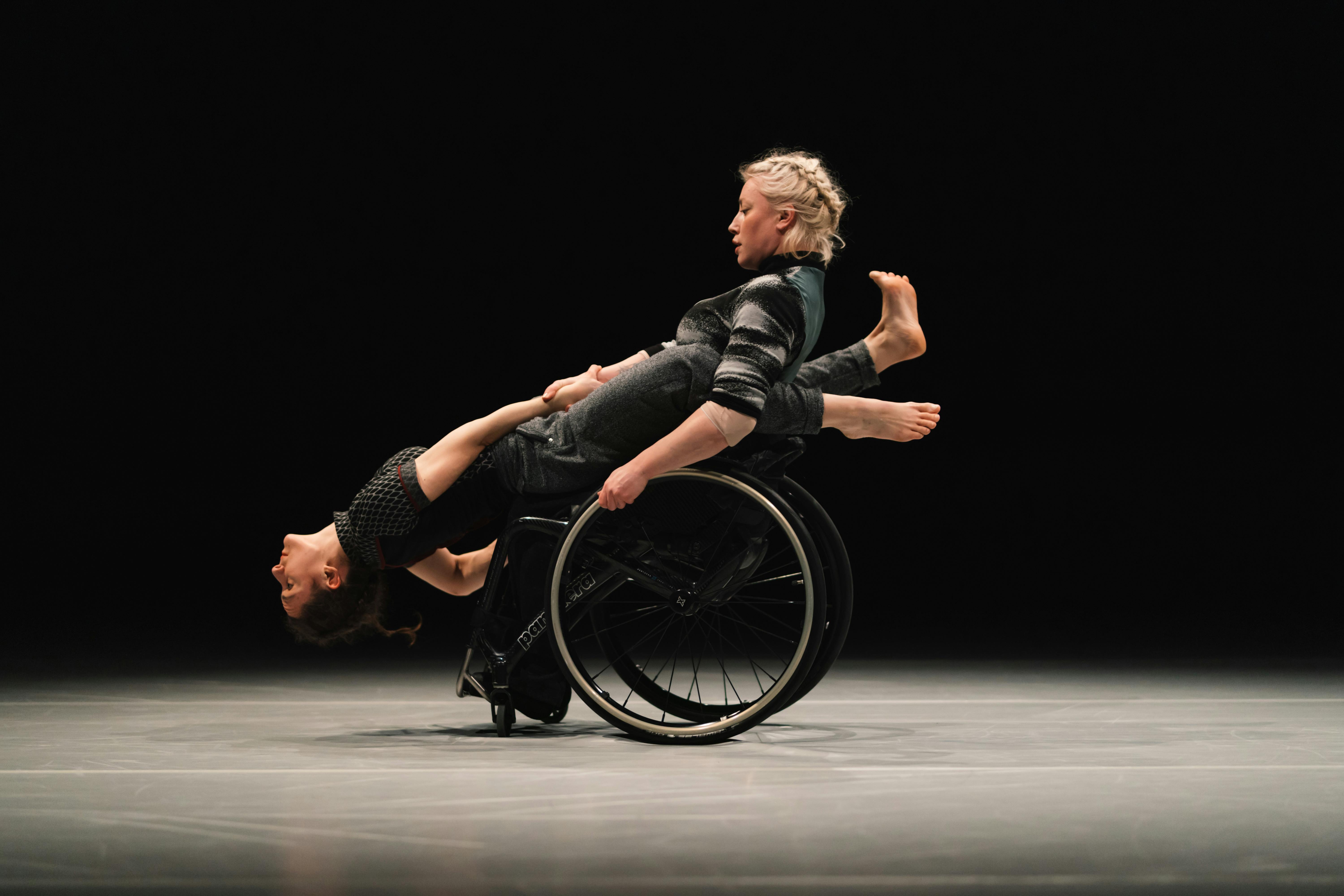 Una danzatrice con disabilità regge in equilibrio perpendicolare un'altra danzatrice.