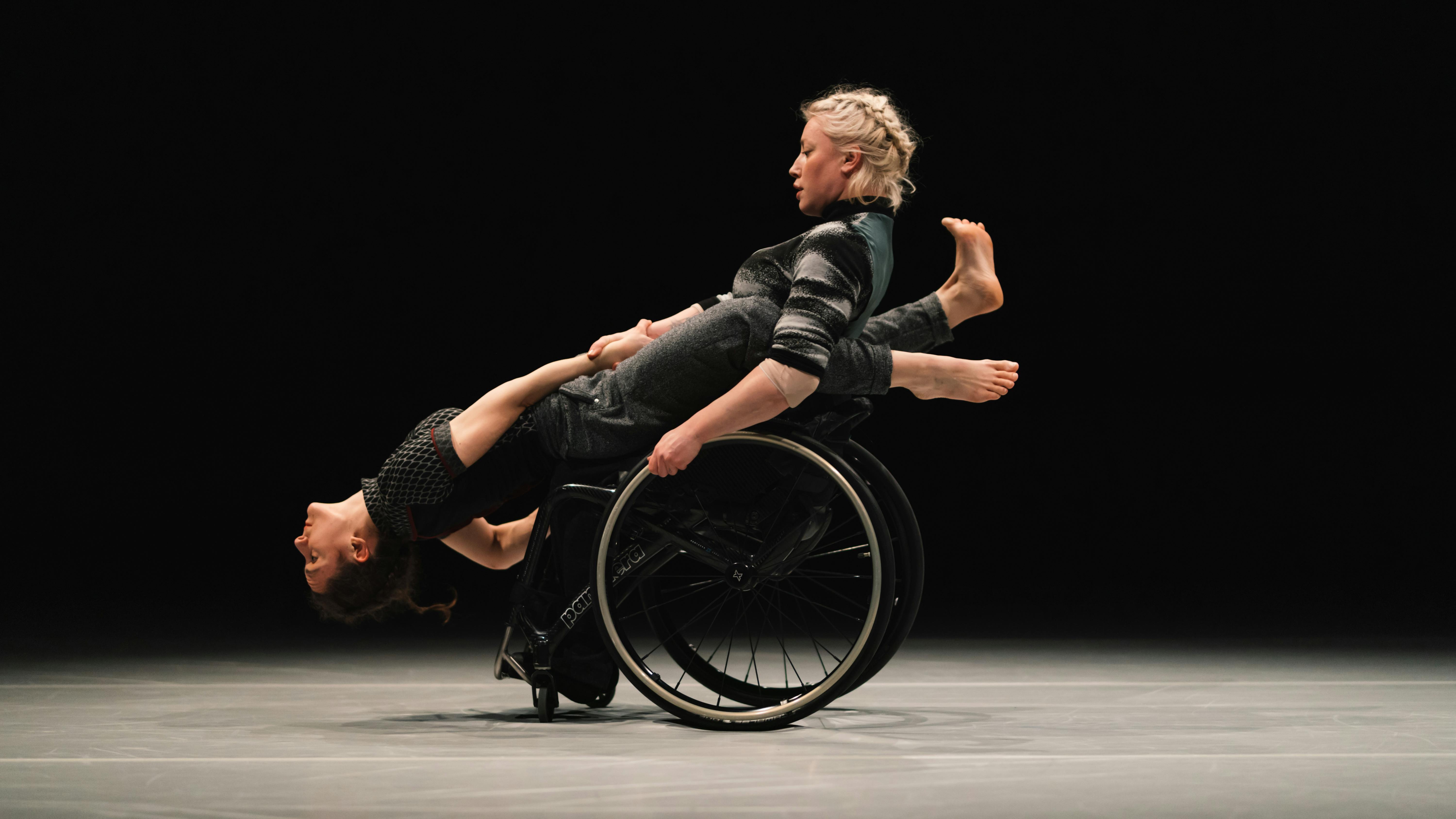 Una danzatrice con disabilità regge in equilibrio perpendicolare un'altra danzatrice.