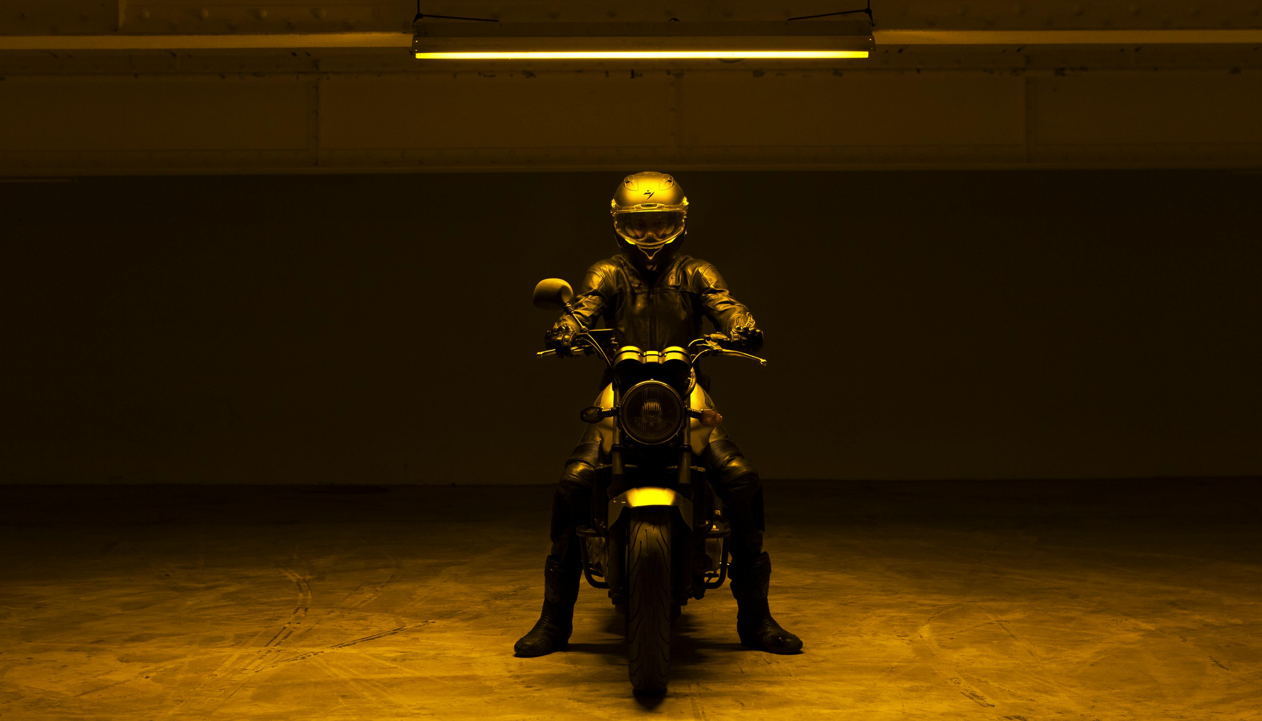 Un motociclista con casco integrale è vestito di nero su una moto al centro di un garage