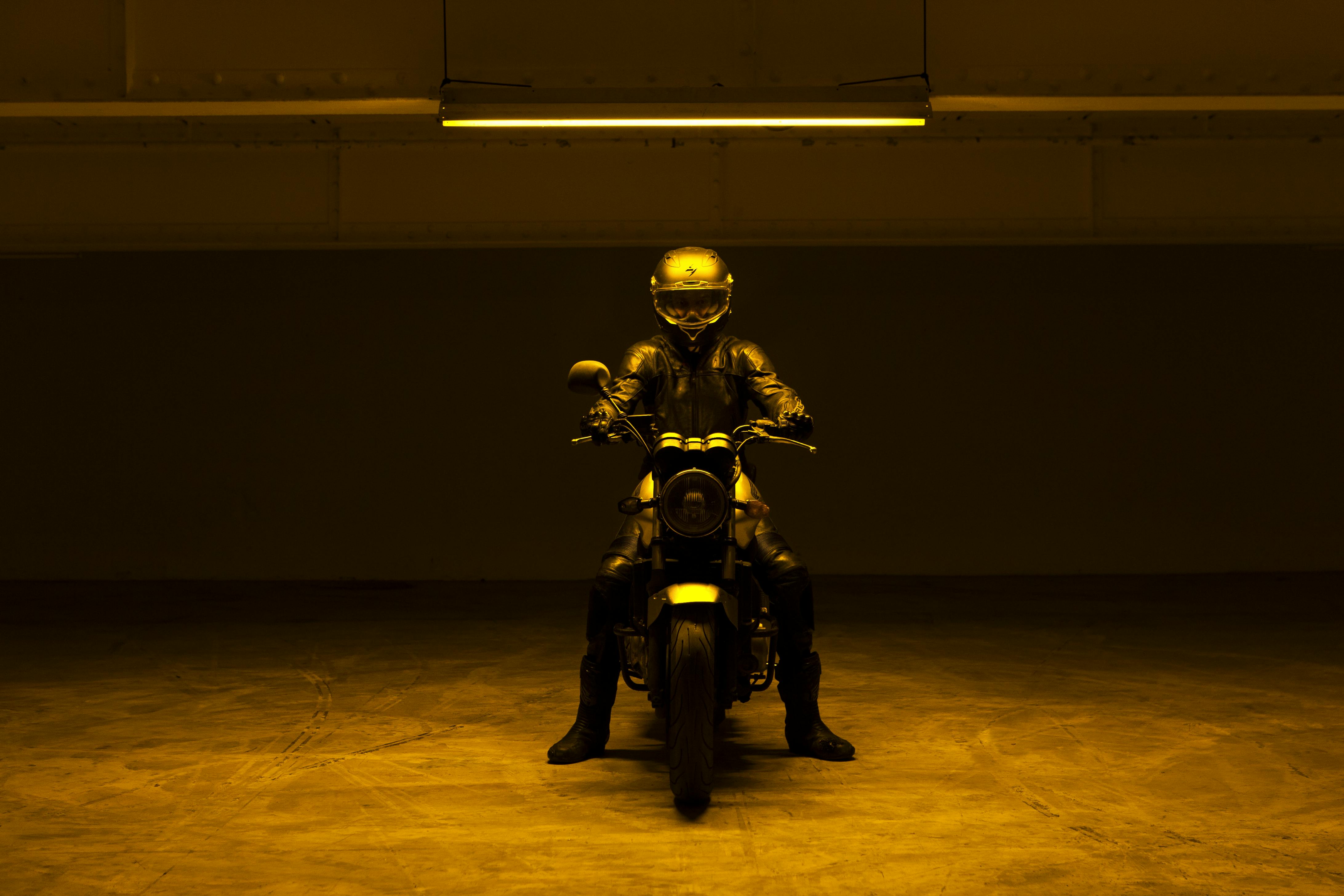 A motorcyclist wearing a full-face helmet is dressed in black on a motorbike in the middle of a garage