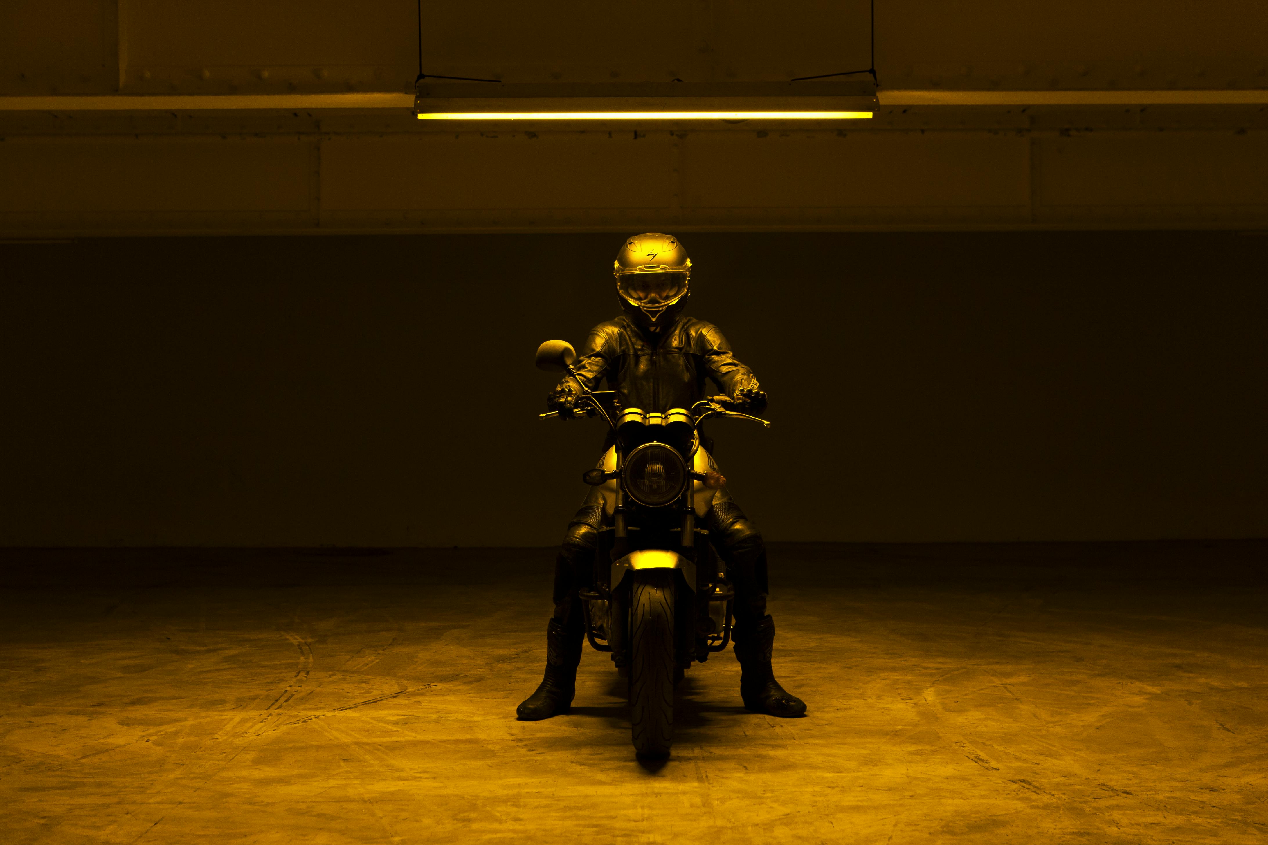 Un motociclista con casco integrale è vestito di nero su una moto al centro di un garage