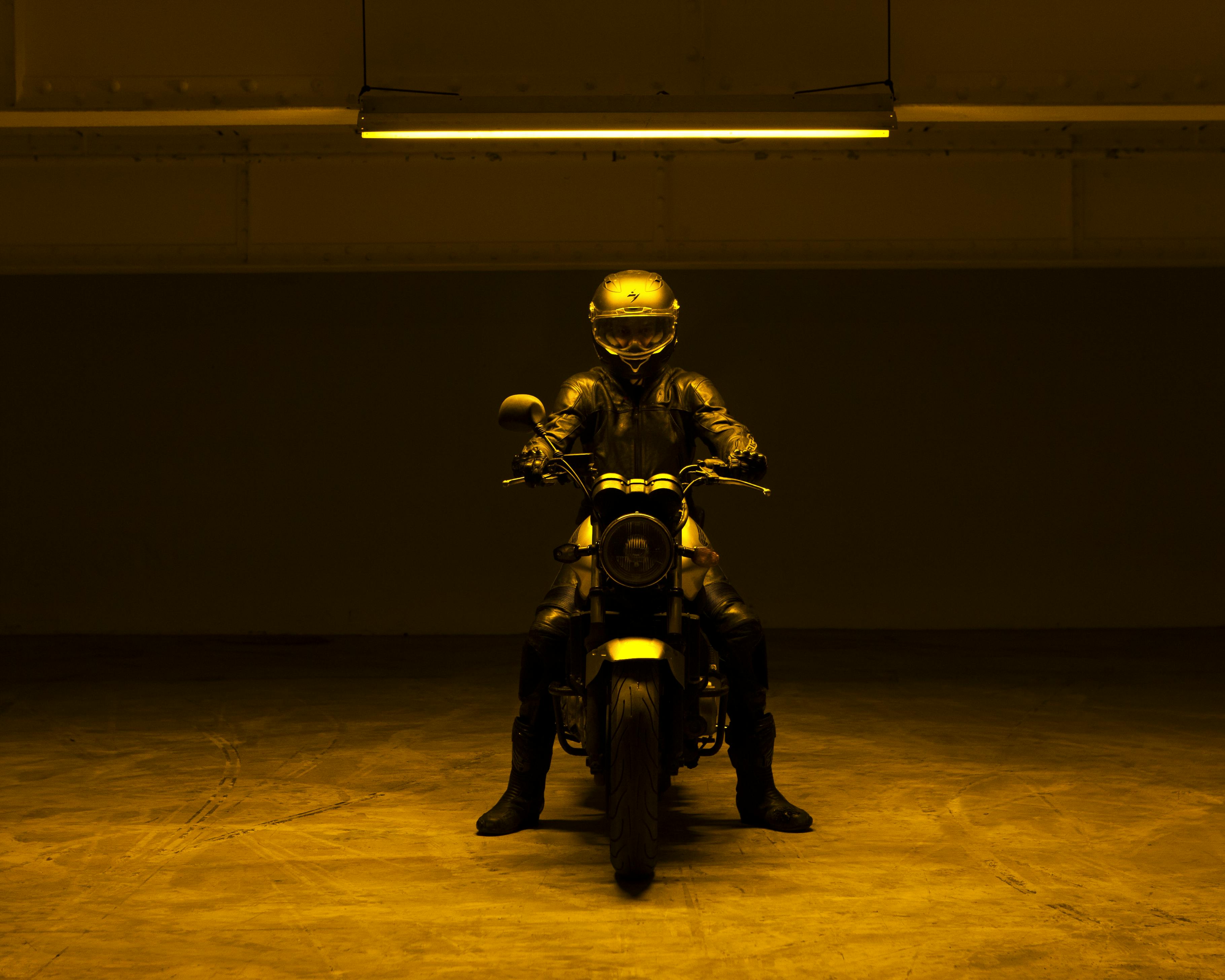 Un motociclista con casco integrale è vestito di nero su una moto al centro di un garage