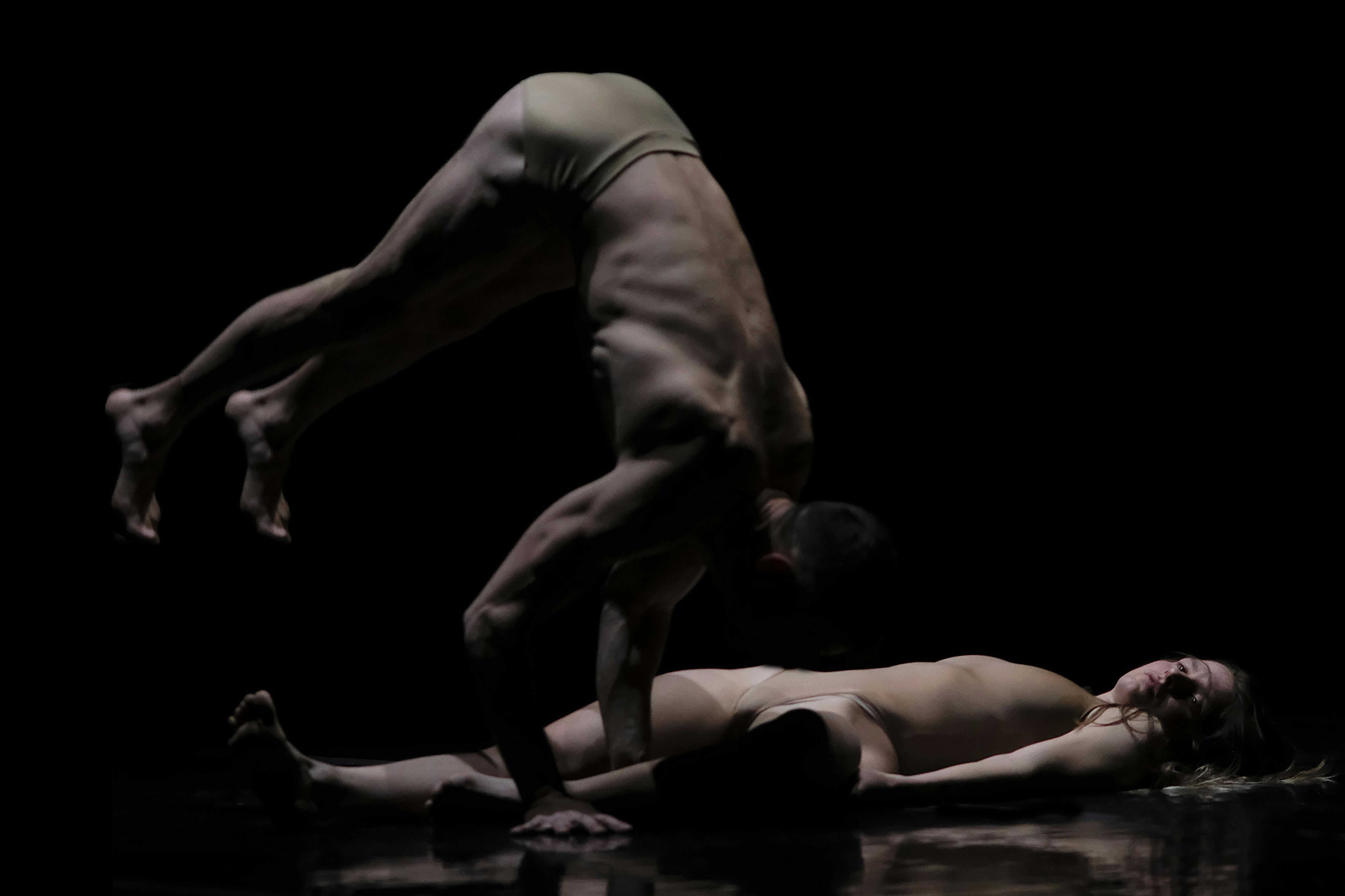 Una danzatrice stesa per terra e un danzatore davanti a lei con il peso sulle braccia.