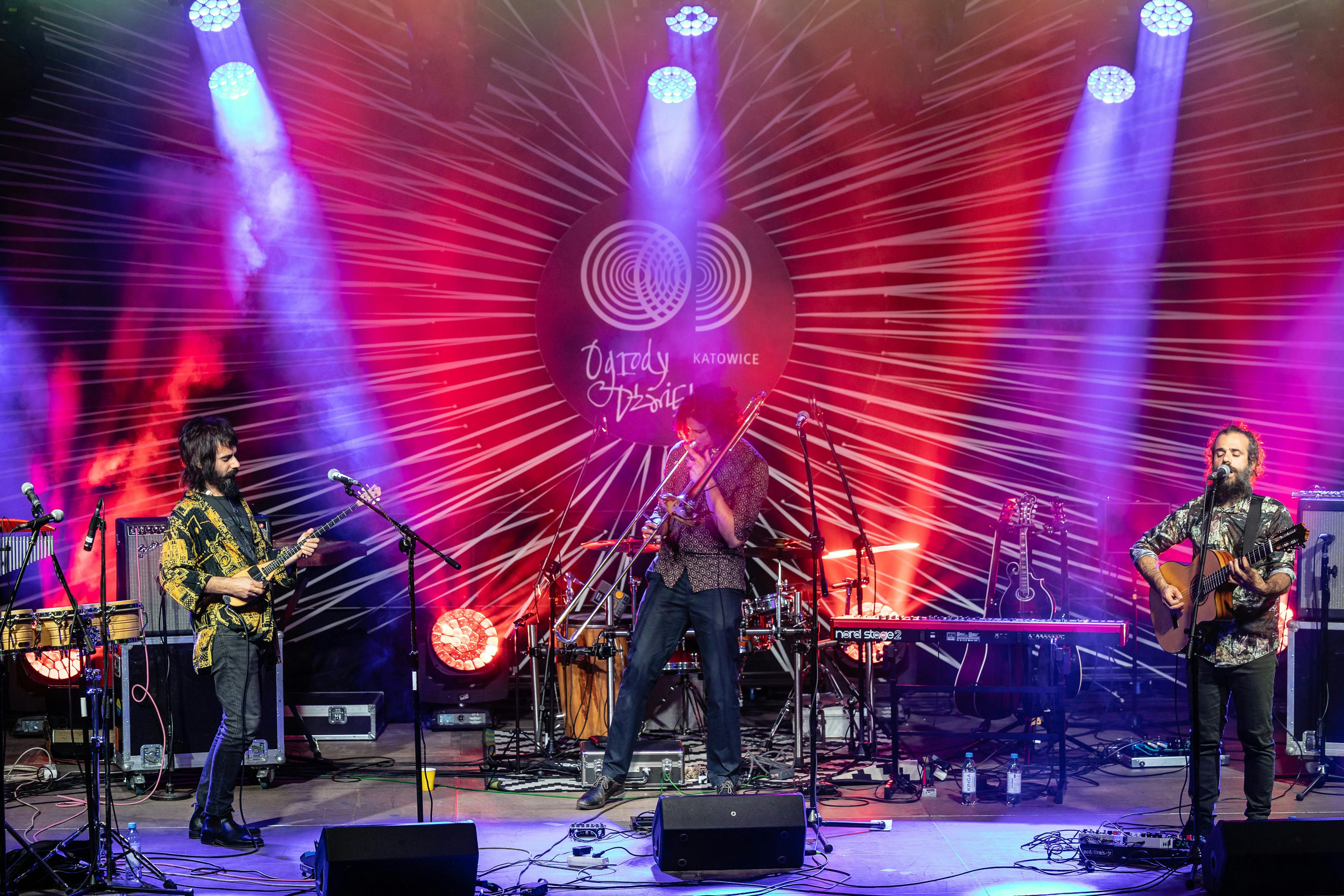 Three musicians on stage with instruments, playing from right to left a tzouras, a trombone and a guitar.